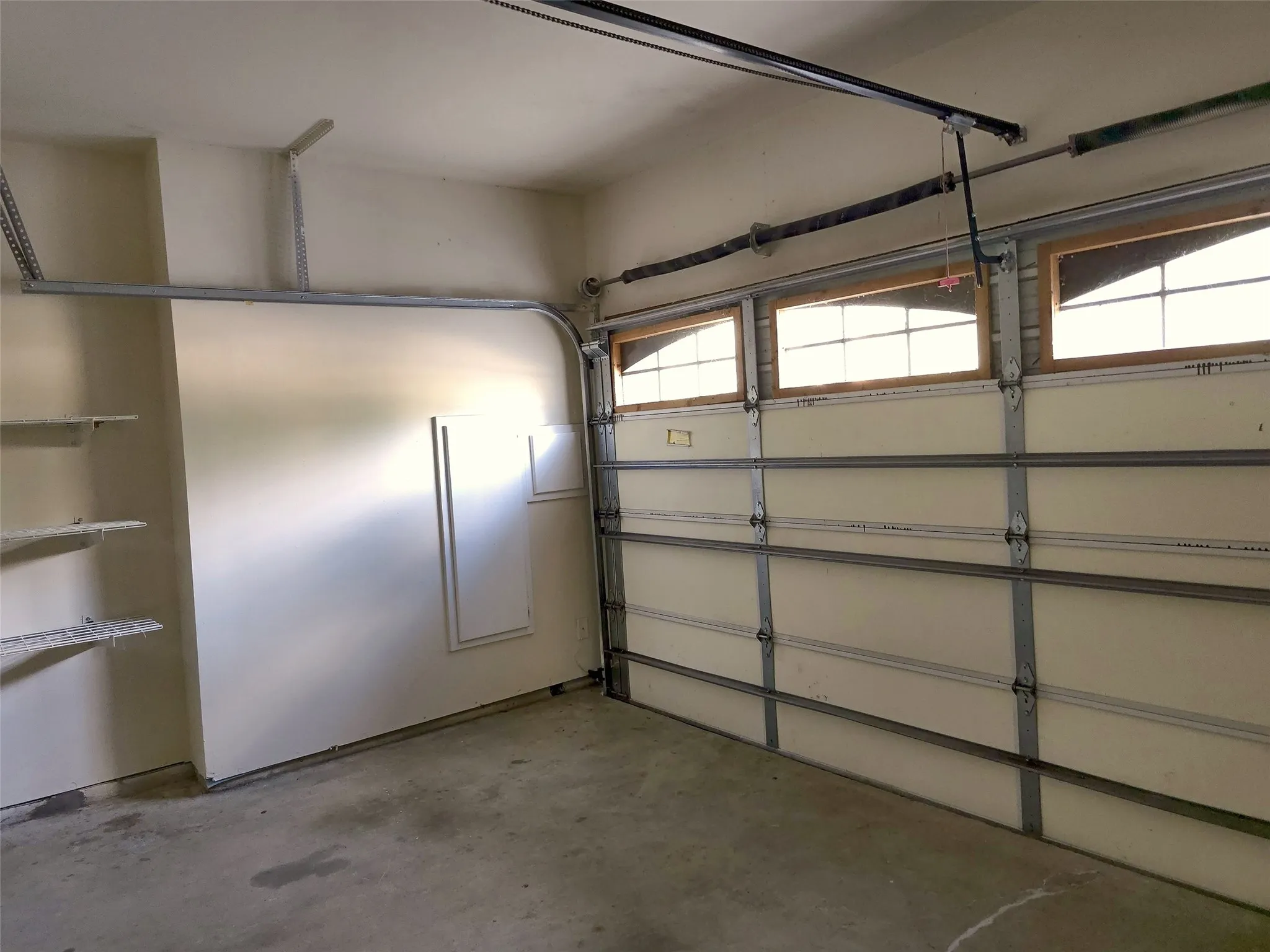 Attached garage with concrete flooring, adjustable wall-mounted shelving, and an overhead garage door featuring integrated windows