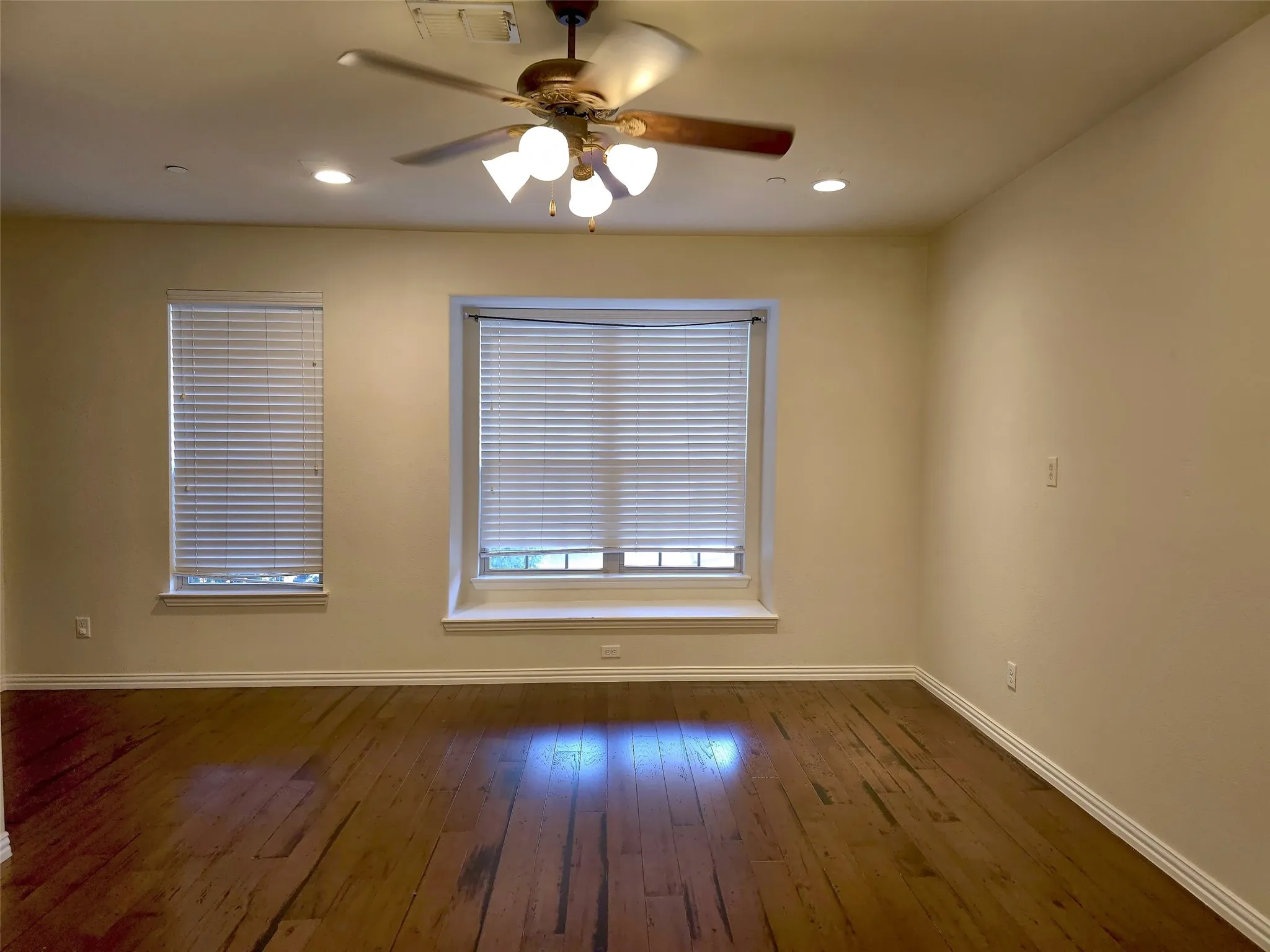 Rich wood-finish flooring, two windows with blinds, ceiling fan with integrated lighting, and recessed ceiling lighting