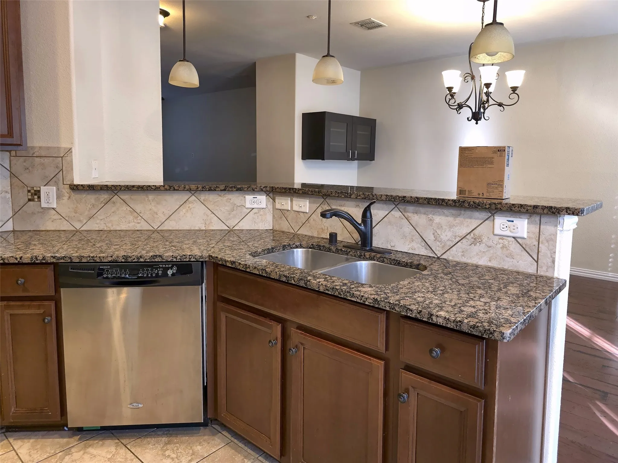 Kitchen featuring granite-style countertops, dual-basin stainless steel sink with a dark-finish faucet, tile backsplash, stainless steel dishwasher, and wooden cabinetry