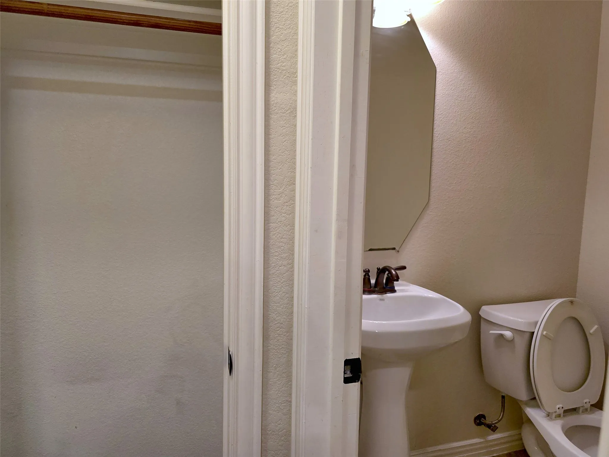 Pedestal sink with bronze-finish faucet, wall-mounted mirror, and toilet