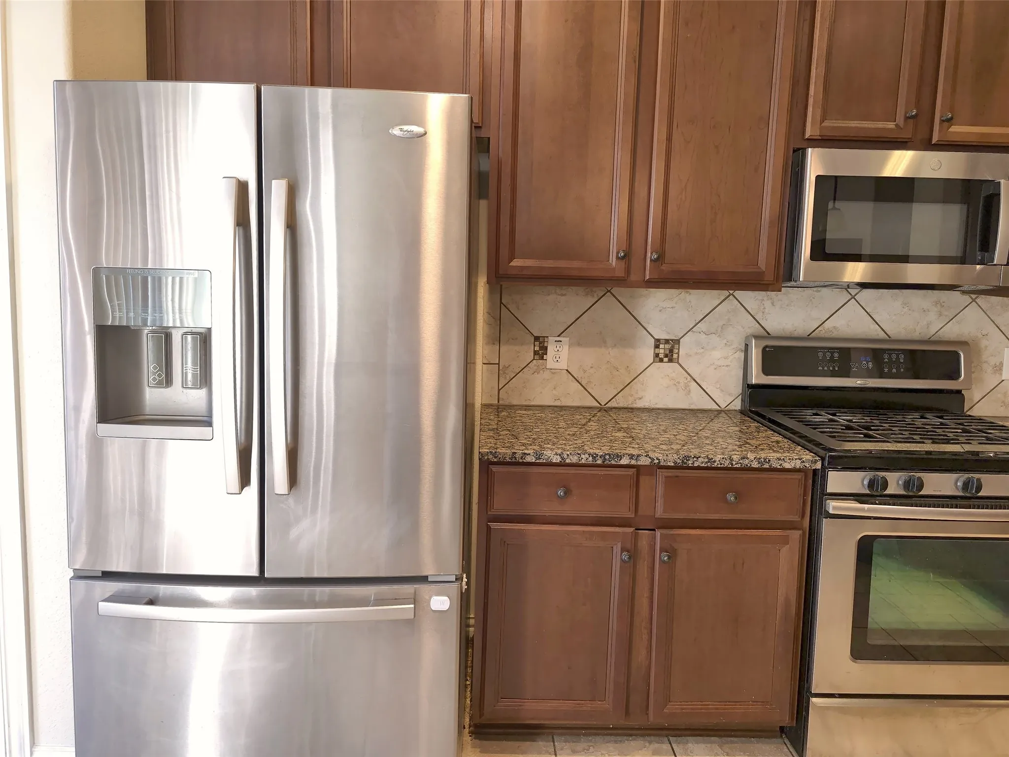Stainless steel French door refrigerator, stainless steel microwave, stainless steel range, granite countertops, and wood cabinetry