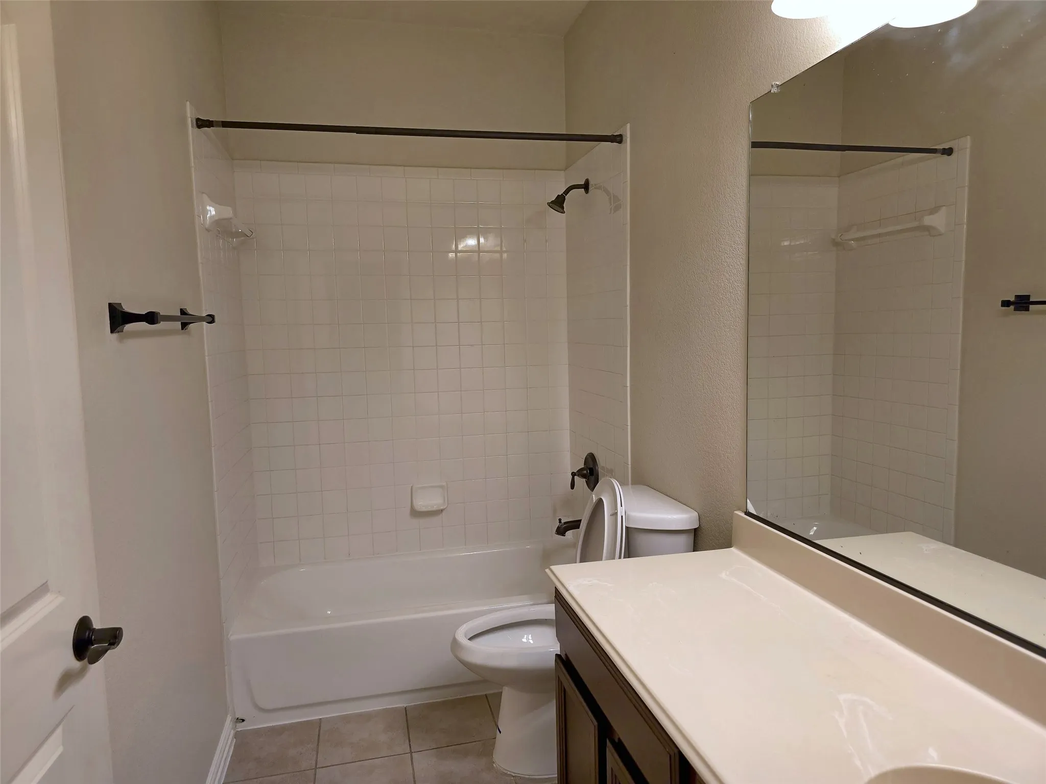 White subway tile shower surround with a built-in tub, dark bronze fixtures, and a vanity with a light-toned countertop