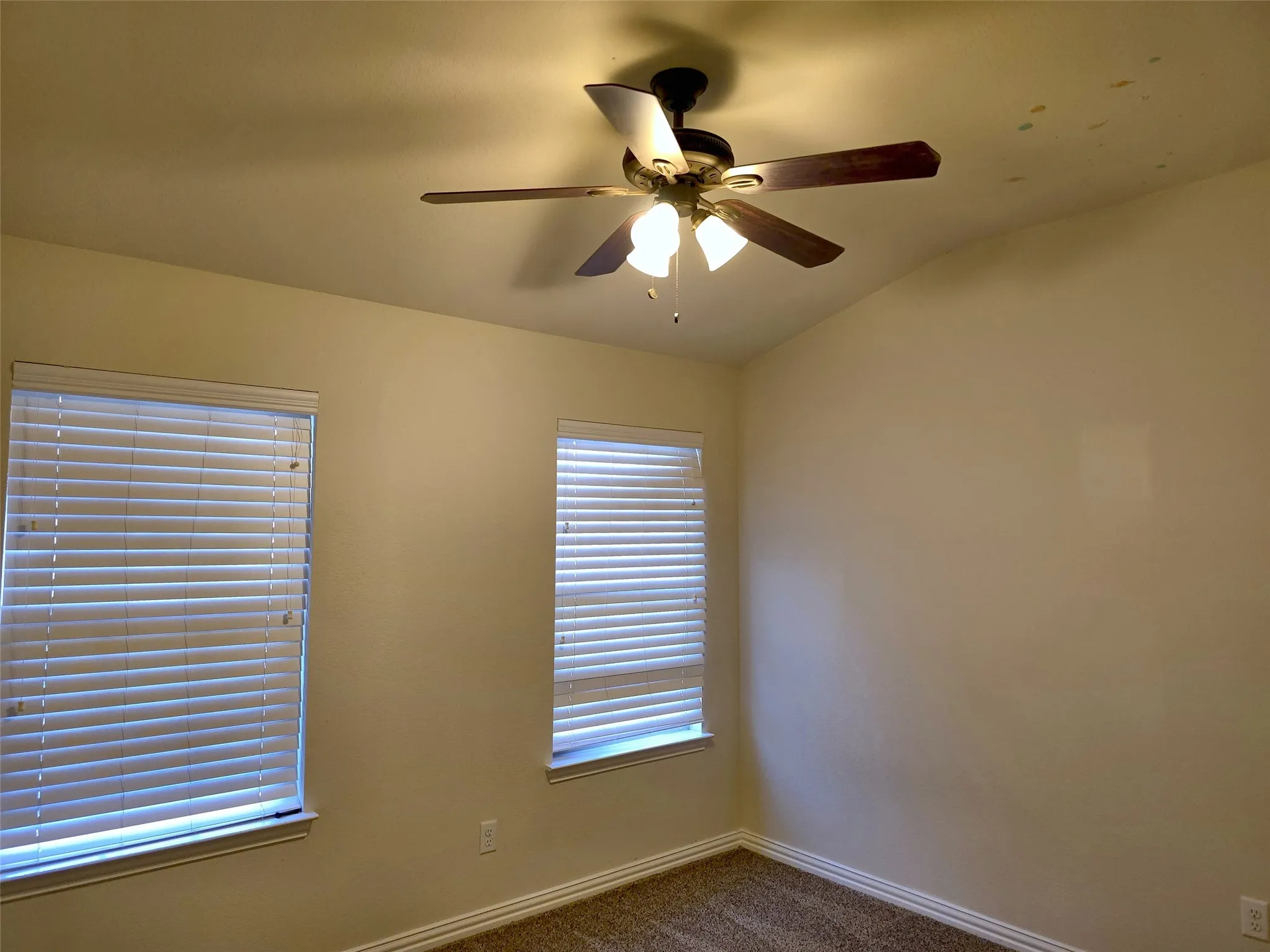 Vaulted ceiling with an attached ceiling fan, two windows with blinds, and neutral wall tones