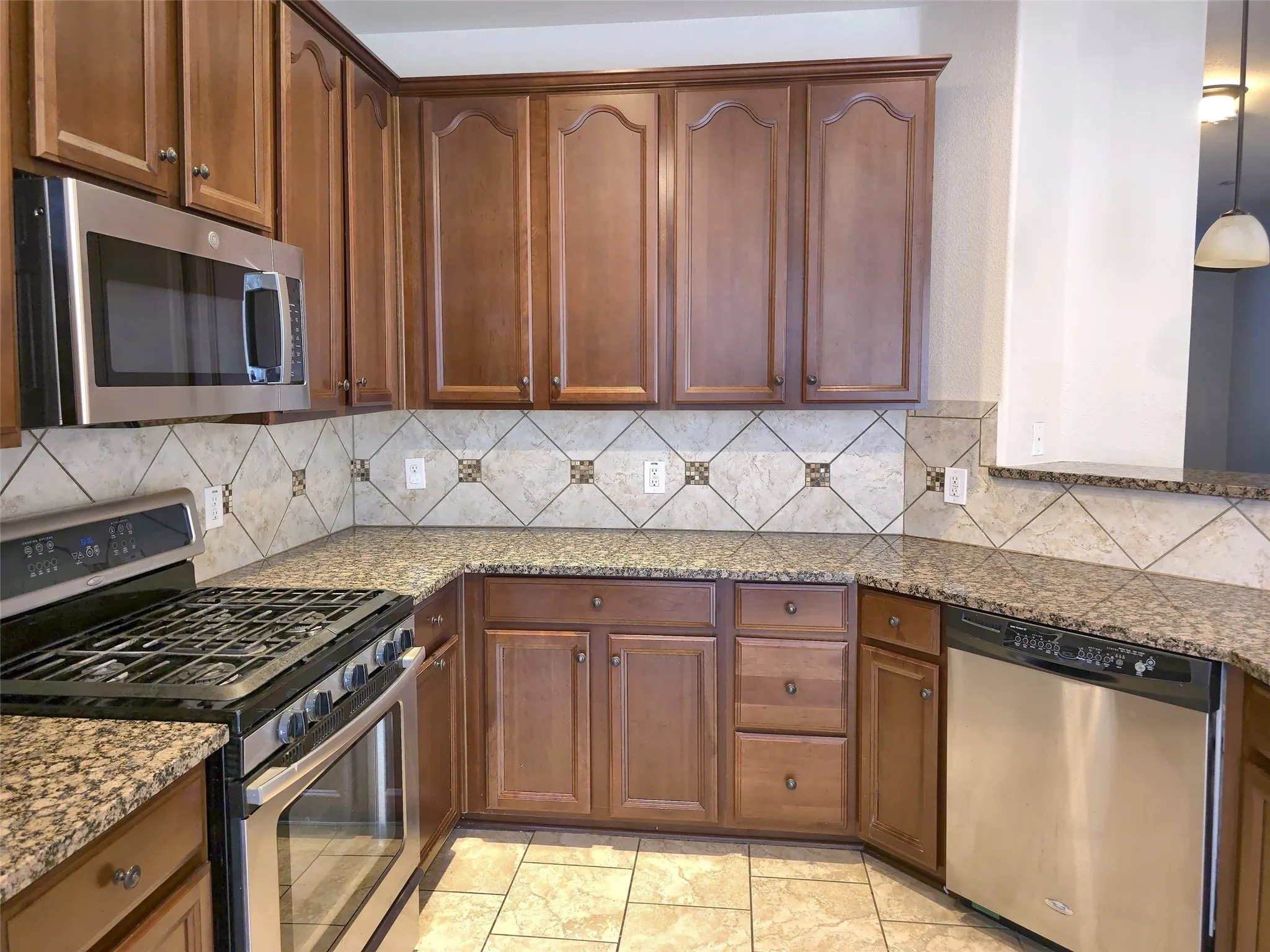 Kitchen featuring wood cabinetry, stainless steel appliances, speckled countertops, and a tiled backsplash