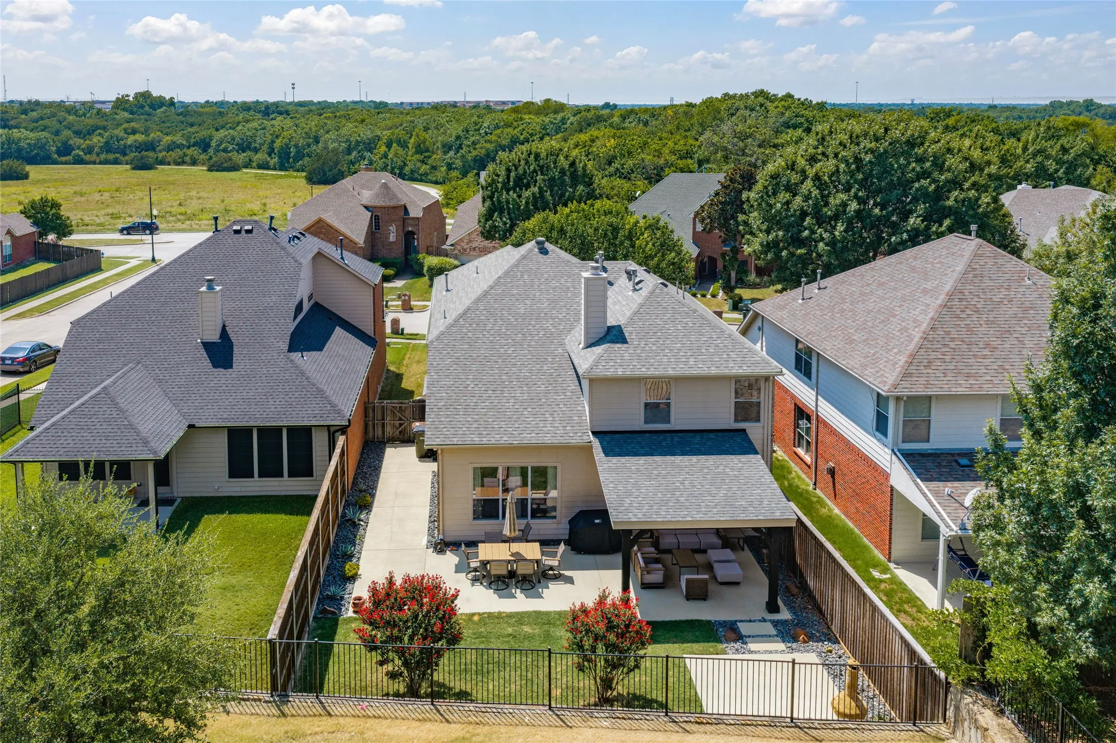 Aerial view of back of the property showing off the Expansive backyard featuring a covered patio, a paver patio area, and a black wrought iron fence