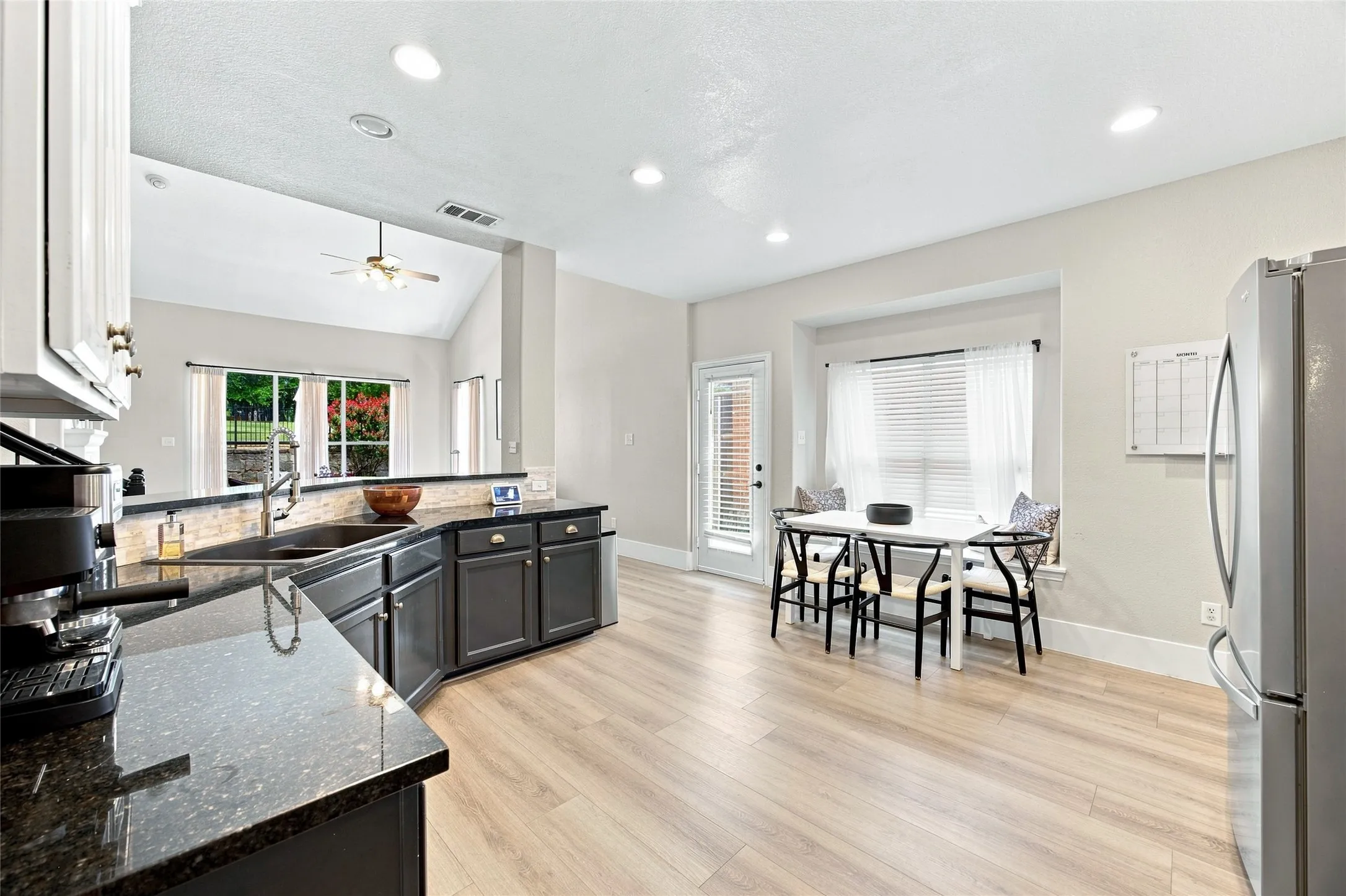 Spacious kitchen featuring dark cabinetry, dark countertops, a tile backsplash, with plenty of gathering space around the breakfast area.  This quaint space has a bench seat located at the back of the breakfast table, perfect as additional seating area.
