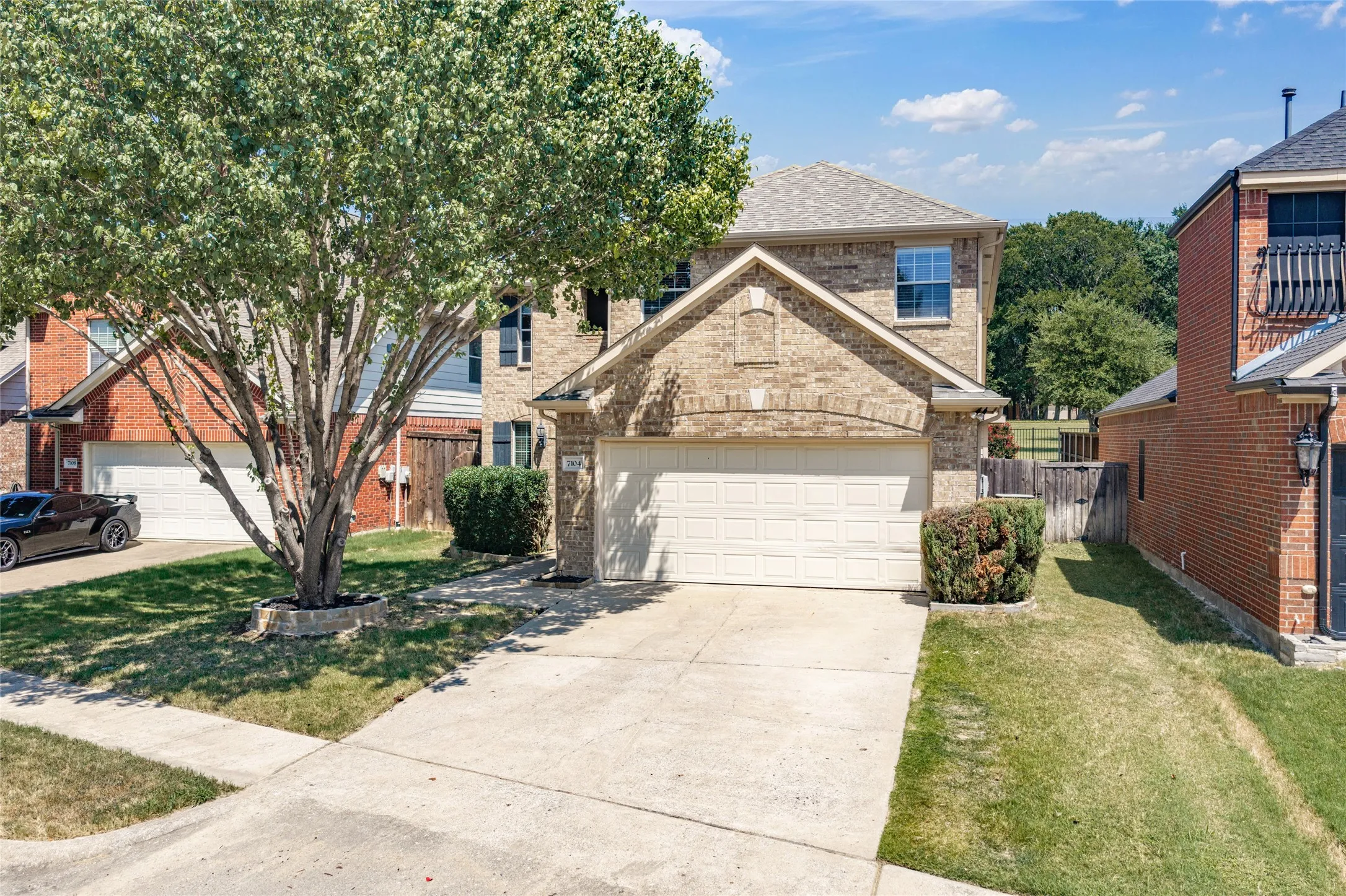 Charming two-story home featuring a brick and stone exterior, white garage door, and mature landscaping including a large shade tree
