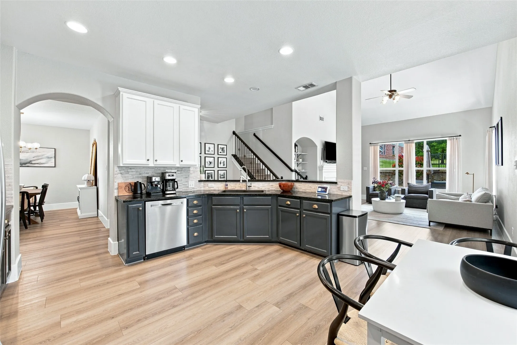 Kitchen featuring two-tone cabinetry, stainless steel dishwasher, wood-finish flooring, and recessed lighting opens to the living room and the formal dining area.