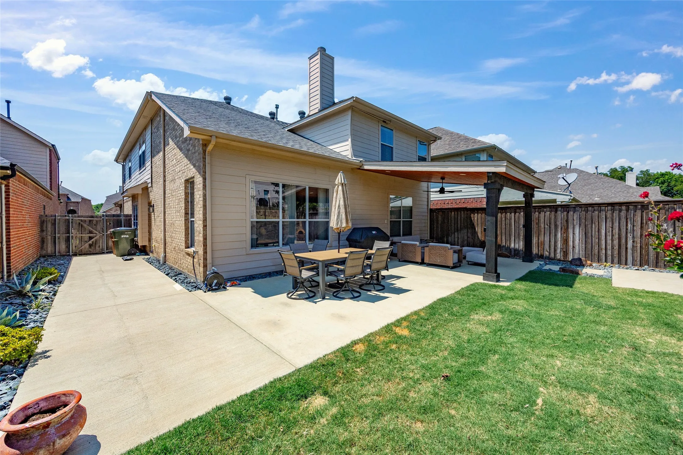 Expansive concrete patio with wide concrete walkway coming directly off the kitchen area of the home leads you to the covered cozy outdoor living area featuring a ceiling fan