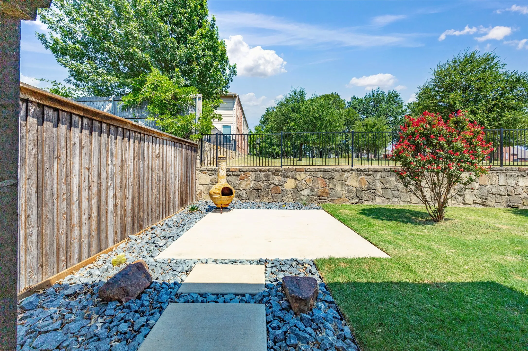 Private backyard featuring a concrete patio, stepping stones, and a stone retaining wall just behind the fire pit area.
