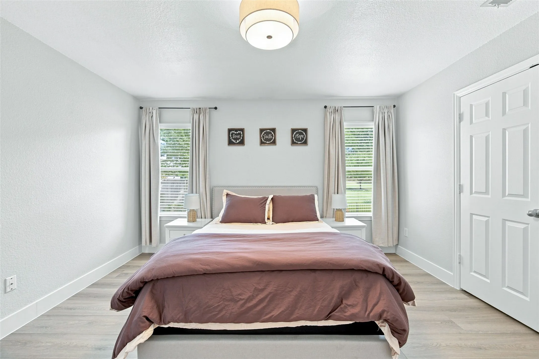 Cozy secondary bedroom great windows with blinds, privacy curtains, spacious closet, light wood-finish flooring,  and a flush mount ceiling light fixture.  Your guest will enjoy this space convienently located just a few steps away from the hallway bathroom.