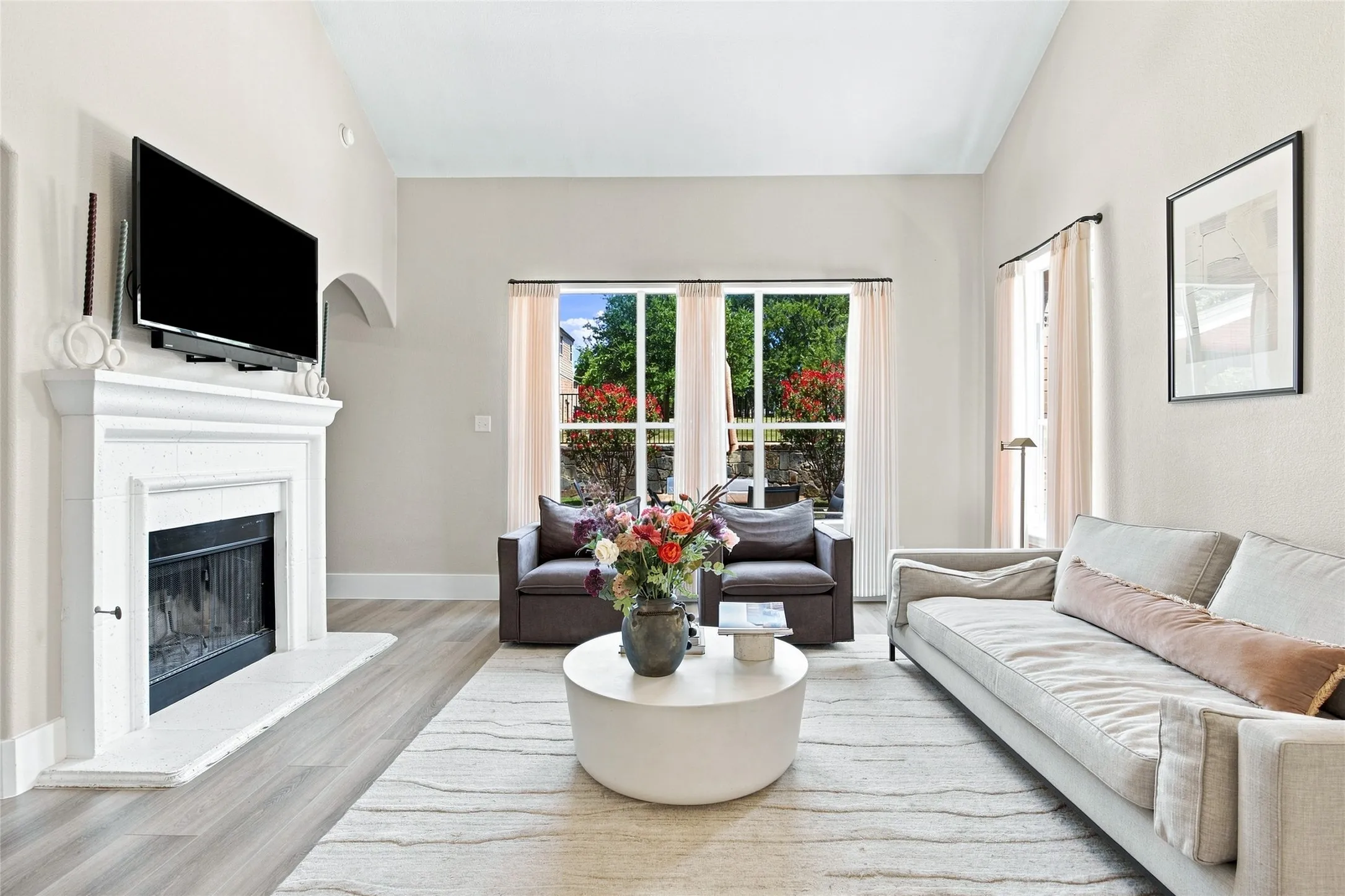 Vaulted ceilings enhance the open cozy living space, featuring a fireplace, wood-finish flooring, and large windows looking out to the backyard area.