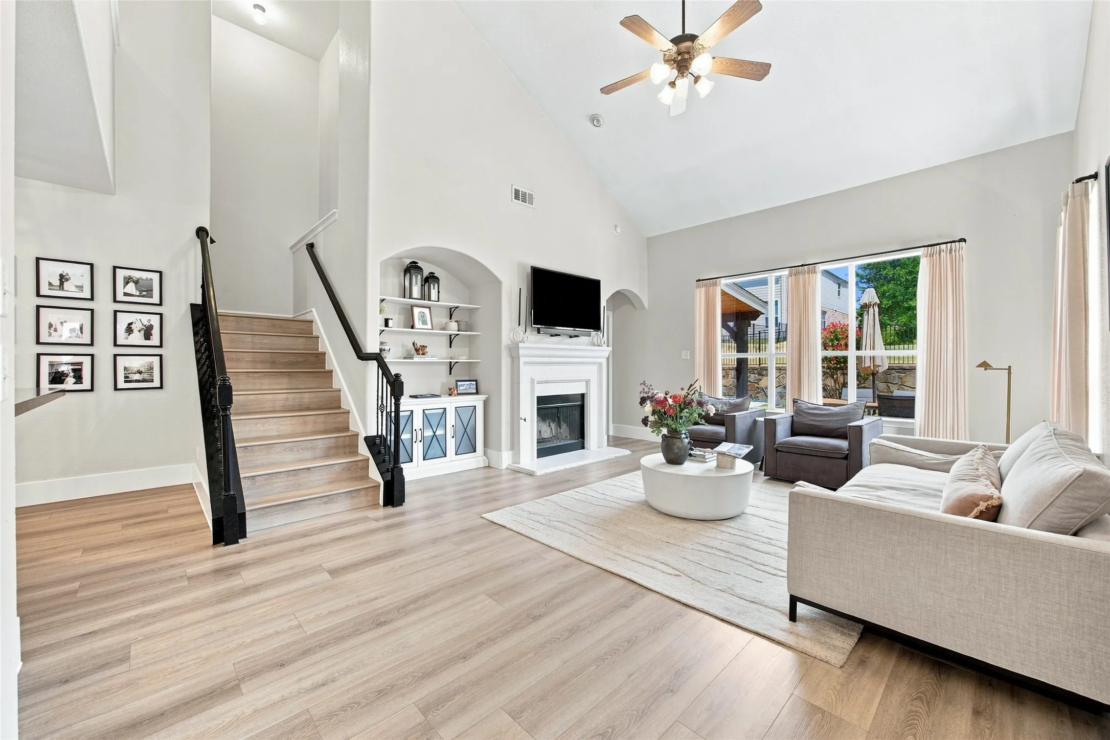 Beautiful inviting living room with Vaulted ceilings, wood-finish flooring, staircase with dark railing, built-in shelving, and a gas fireplace with a mantel.
