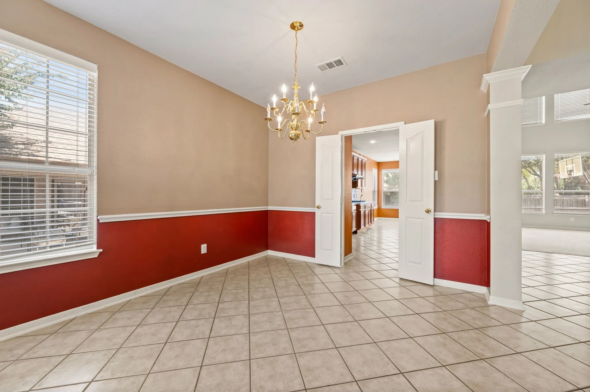 Vaulted ceiling with a gold-tone chandelier, ceramic tile flooring, and a window with blinds