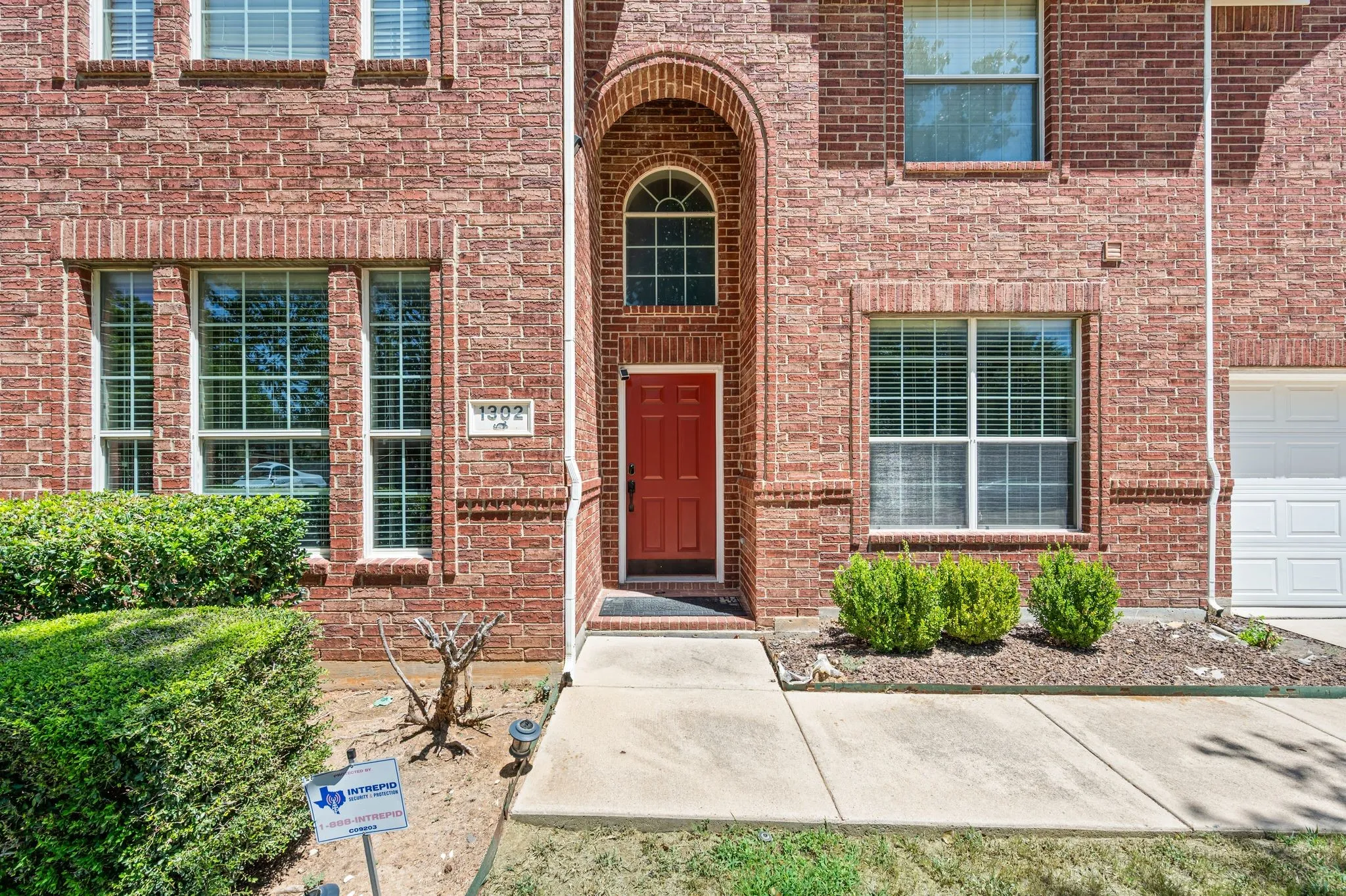 Red brick exterior with an arched entryway, a red entry door, and white-framed windows