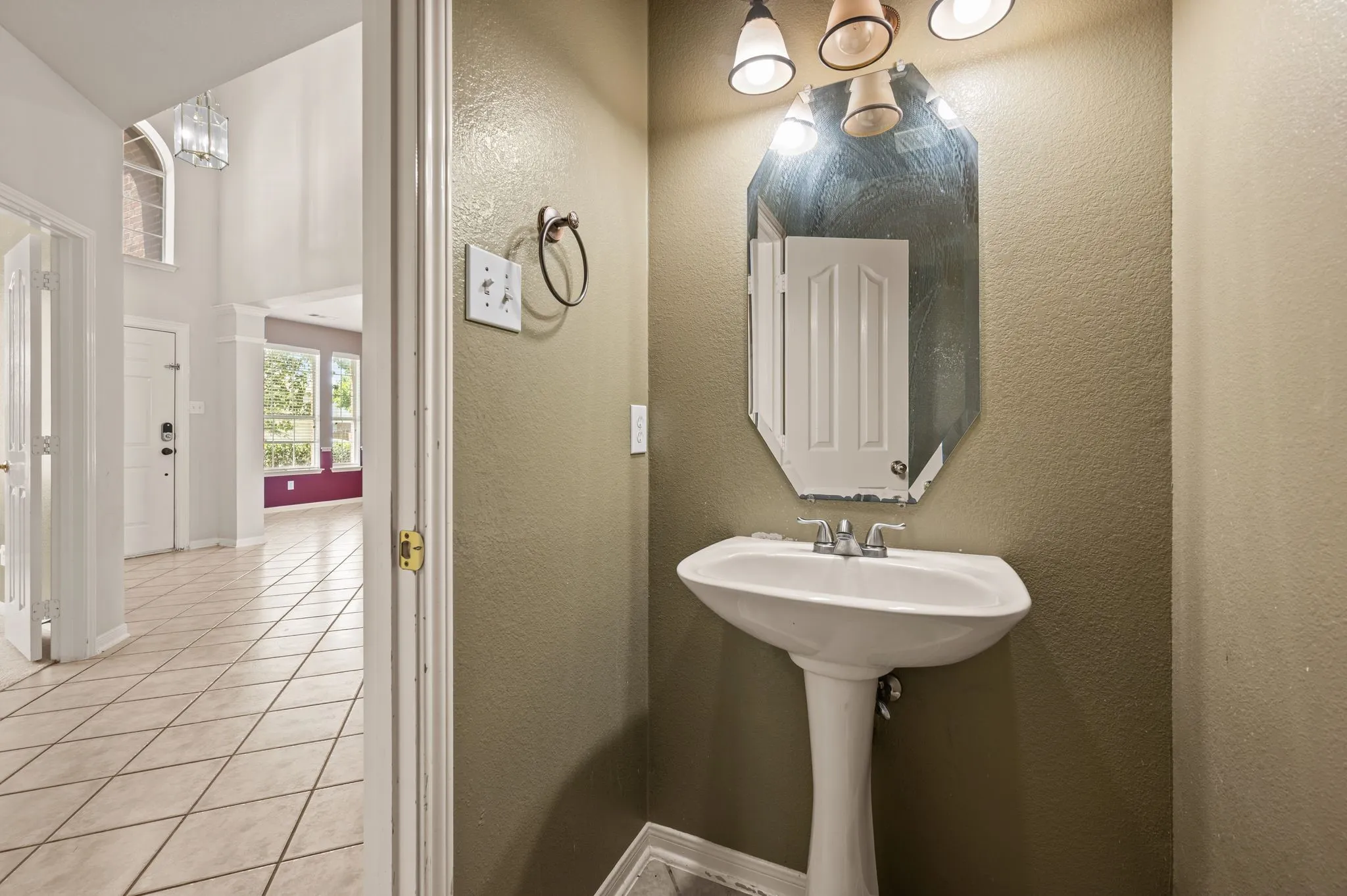 White pedestal sink with a chrome faucet, illuminated by a multi-bulb vanity light fixture