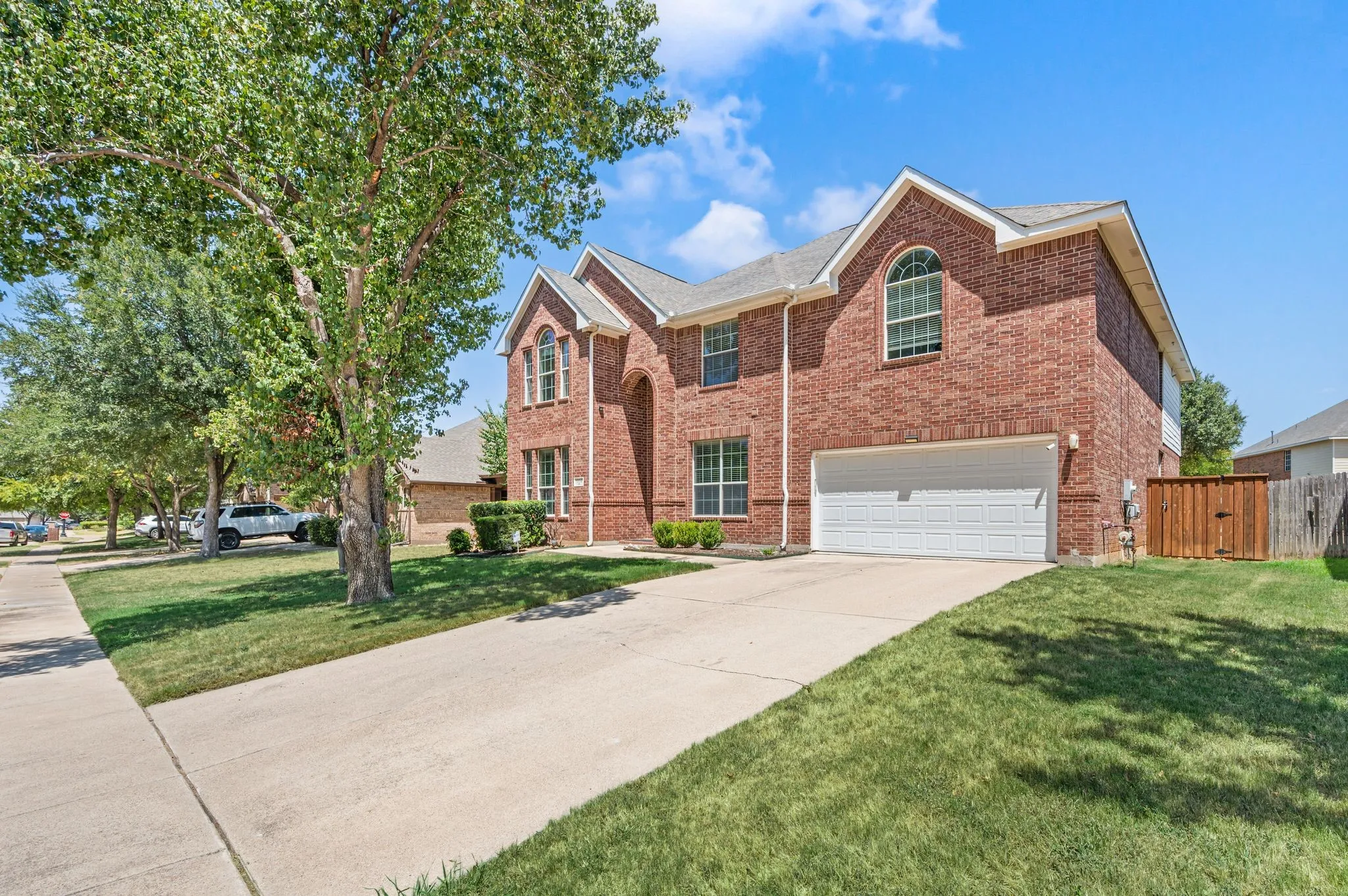 Two-story brick exterior with an arched window, a two-car garage, and mature landscaping
