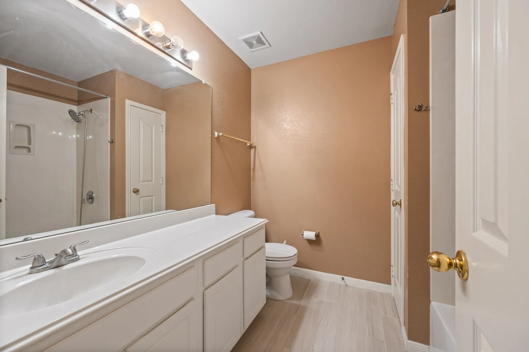 Bathroom featuring a single vanity with an integrated sink, polished chrome faucet, white cabinetry, a full-width mirror, and a shower with a white surround