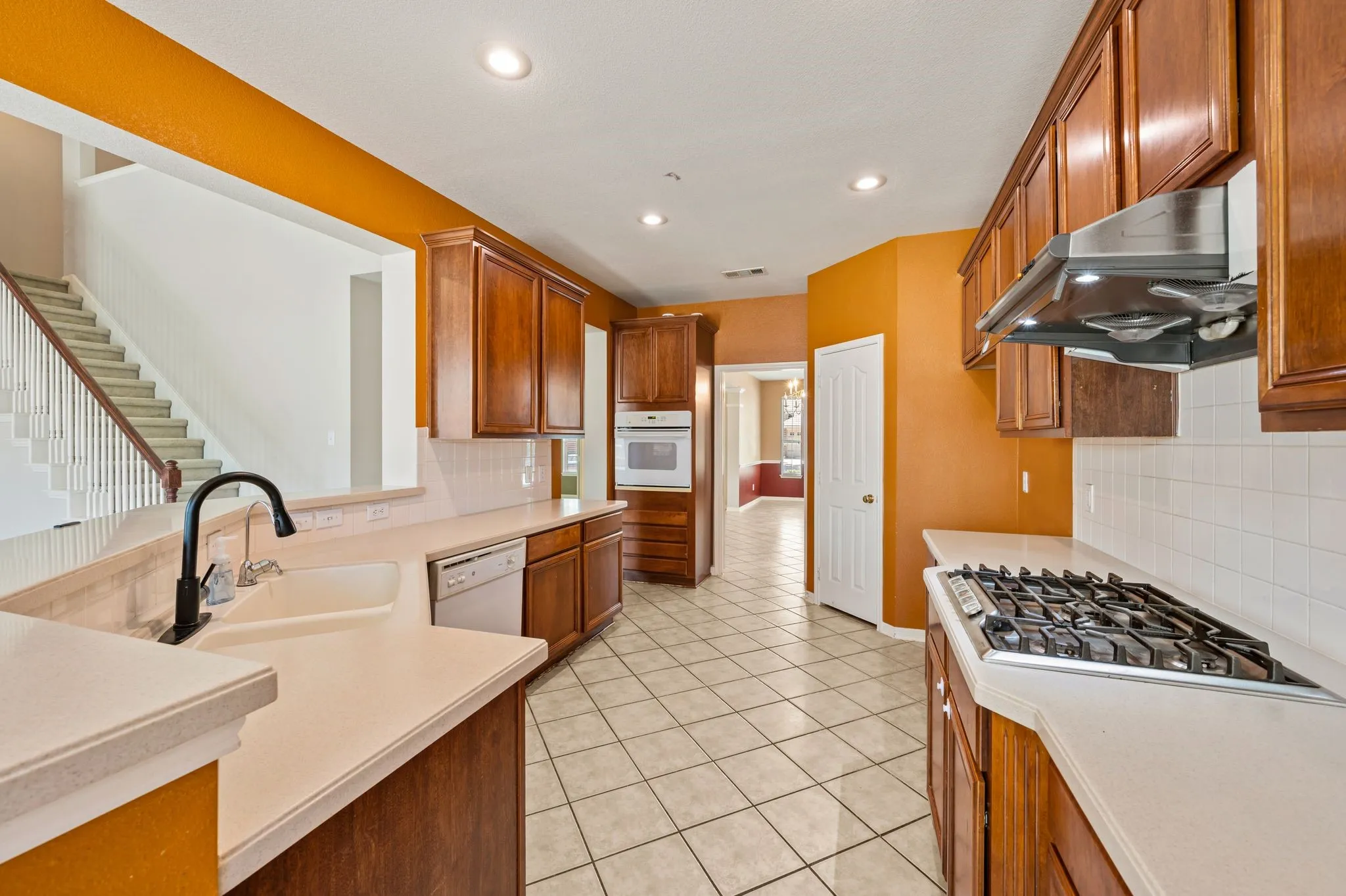 Kitchen featuring wood cabinetry, light countertops, white tile backsplash, a gas range with an overhead vent, and tile flooring