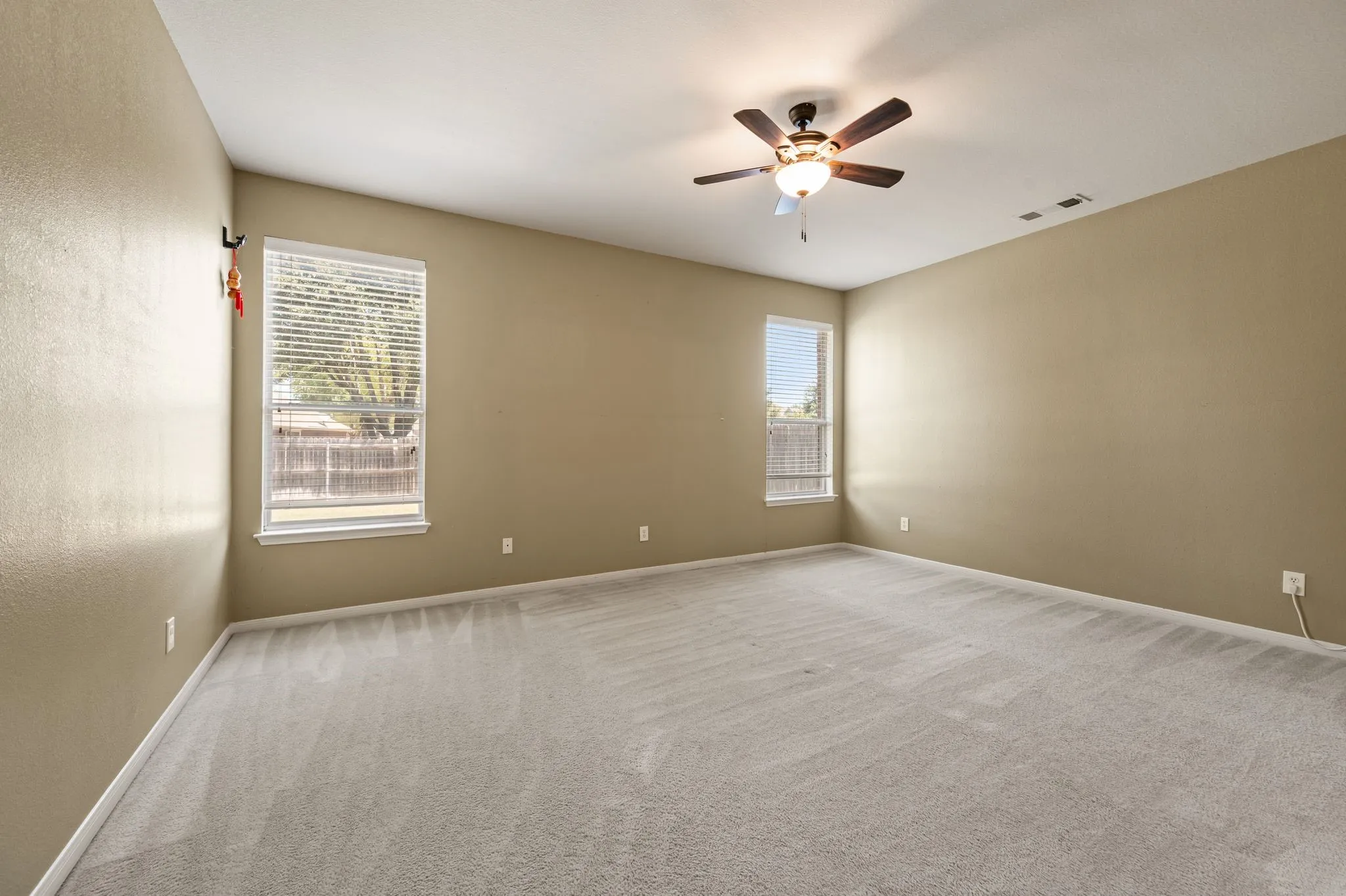 Spacious room featuring neutral carpeting, a ceiling fan with integrated lighting, and dual windows