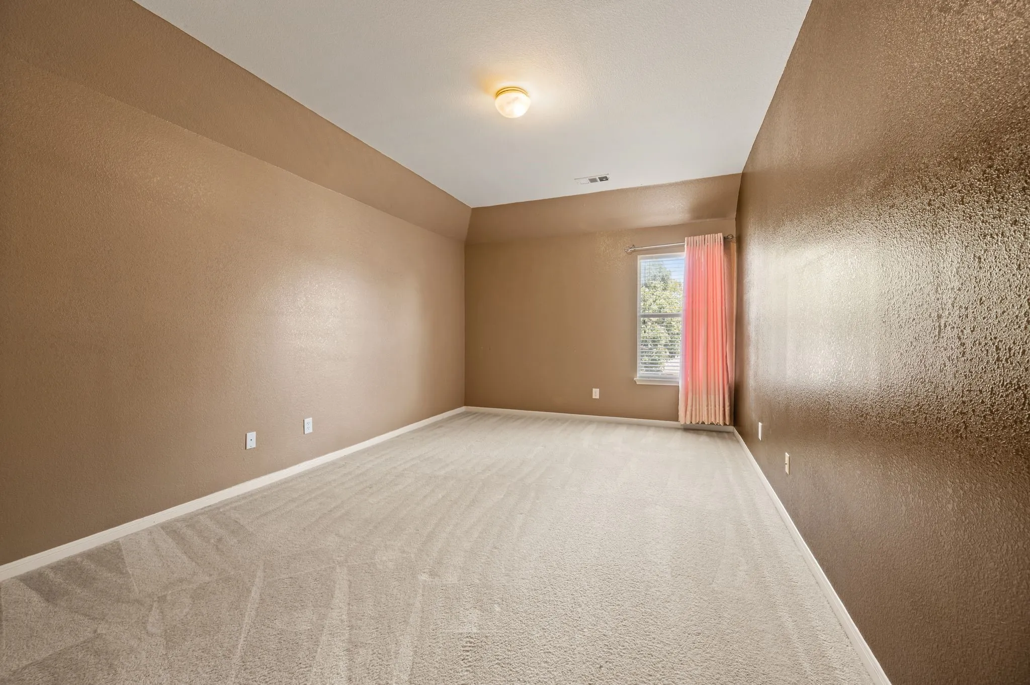 Vaulted ceiling, ceiling-mounted light fixture, light-colored carpeting, window with privacy treatments, and neutral wall tones