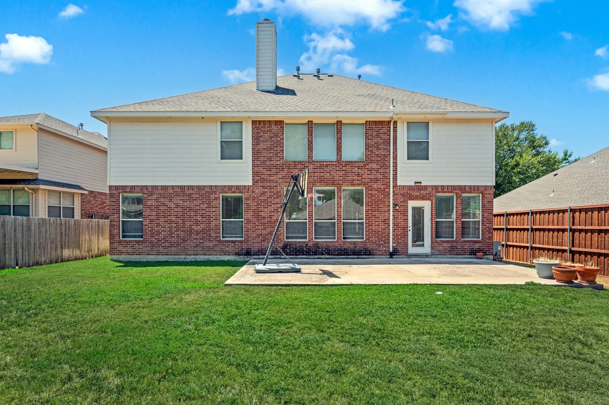 Backyard featuring a red brick and white siding exterior, a concrete patio, a wood privacy fence, and a chimney