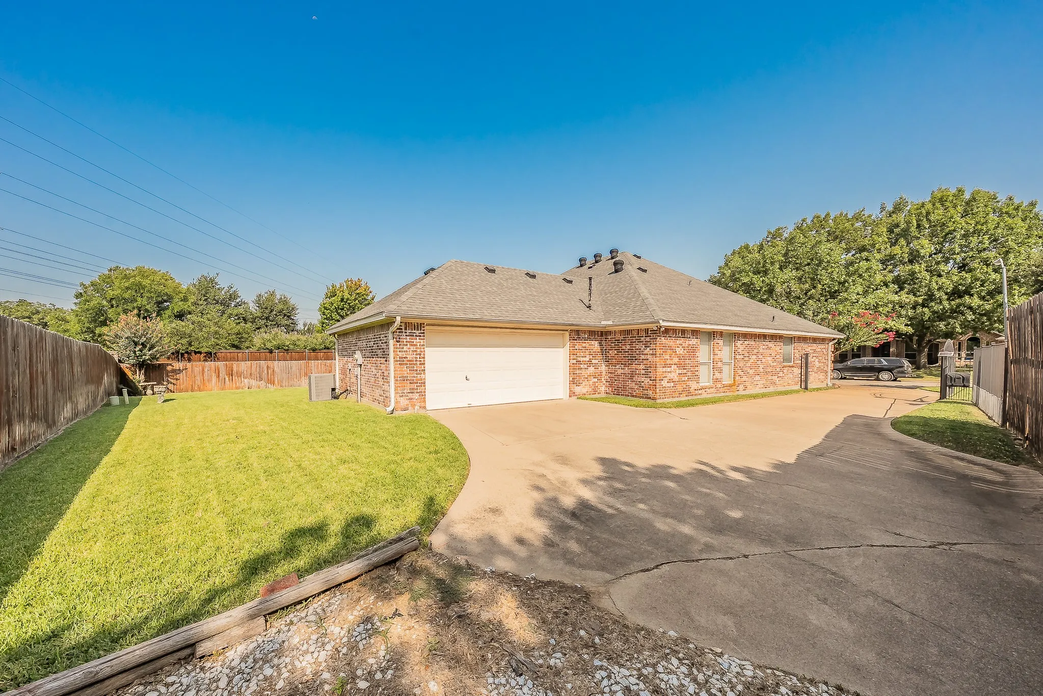 Traditional brick exterior with an attached garage, paved driveway, and a fenced backyard featuring a grassy lawn