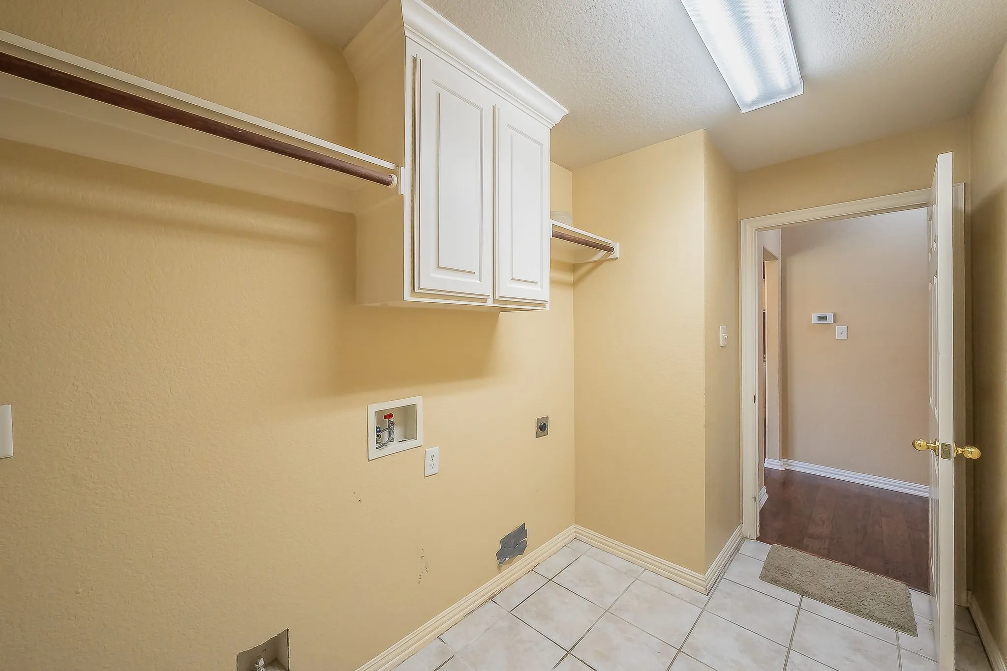 Tile flooring, white cabinetry with crown molding, wall-mounted clothes rod, and a fluorescent ceiling light fixture