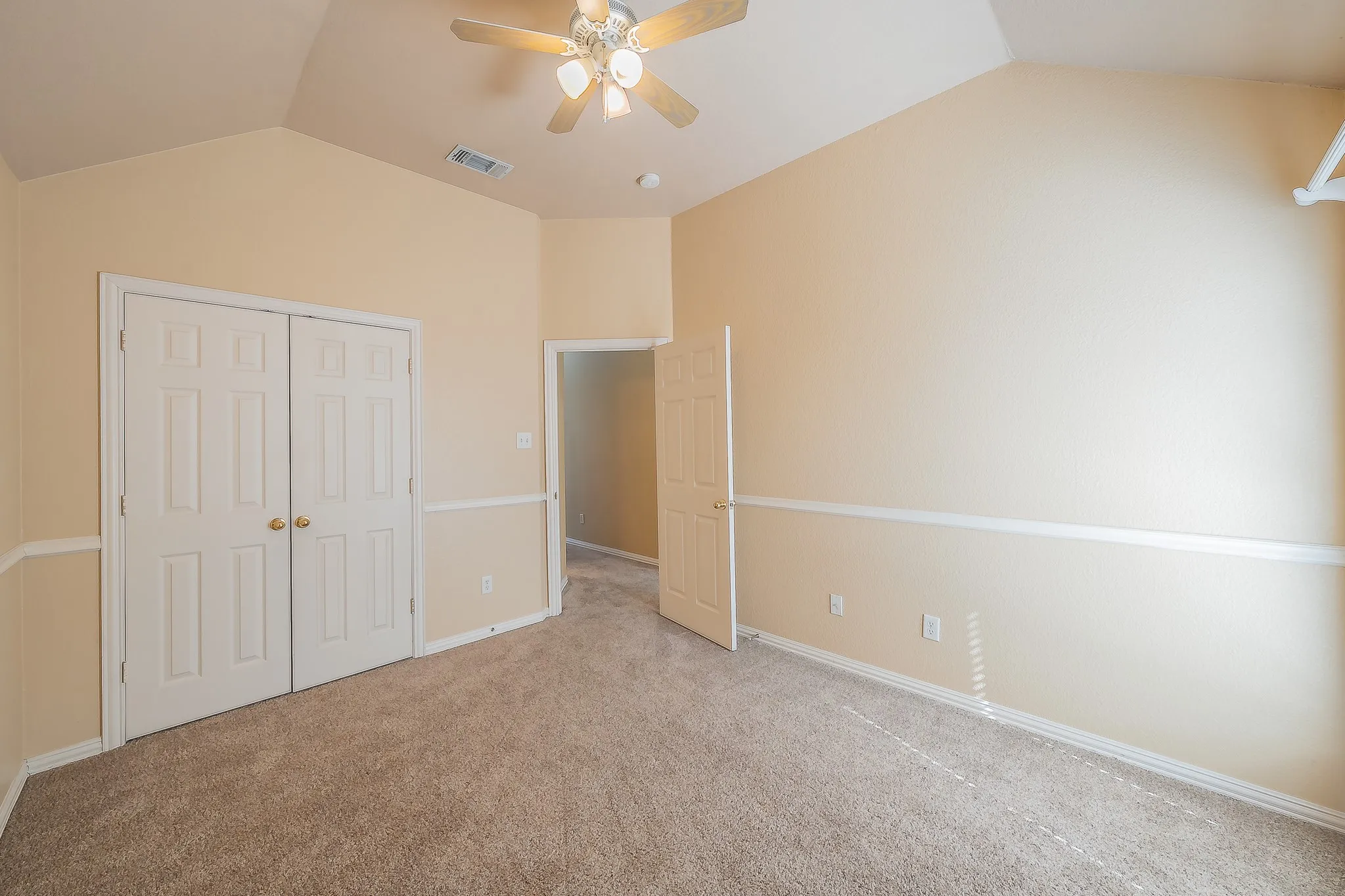 Vaulted ceiling with a ceiling fan, neutral wall paint, carpet flooring, and a six-panel door