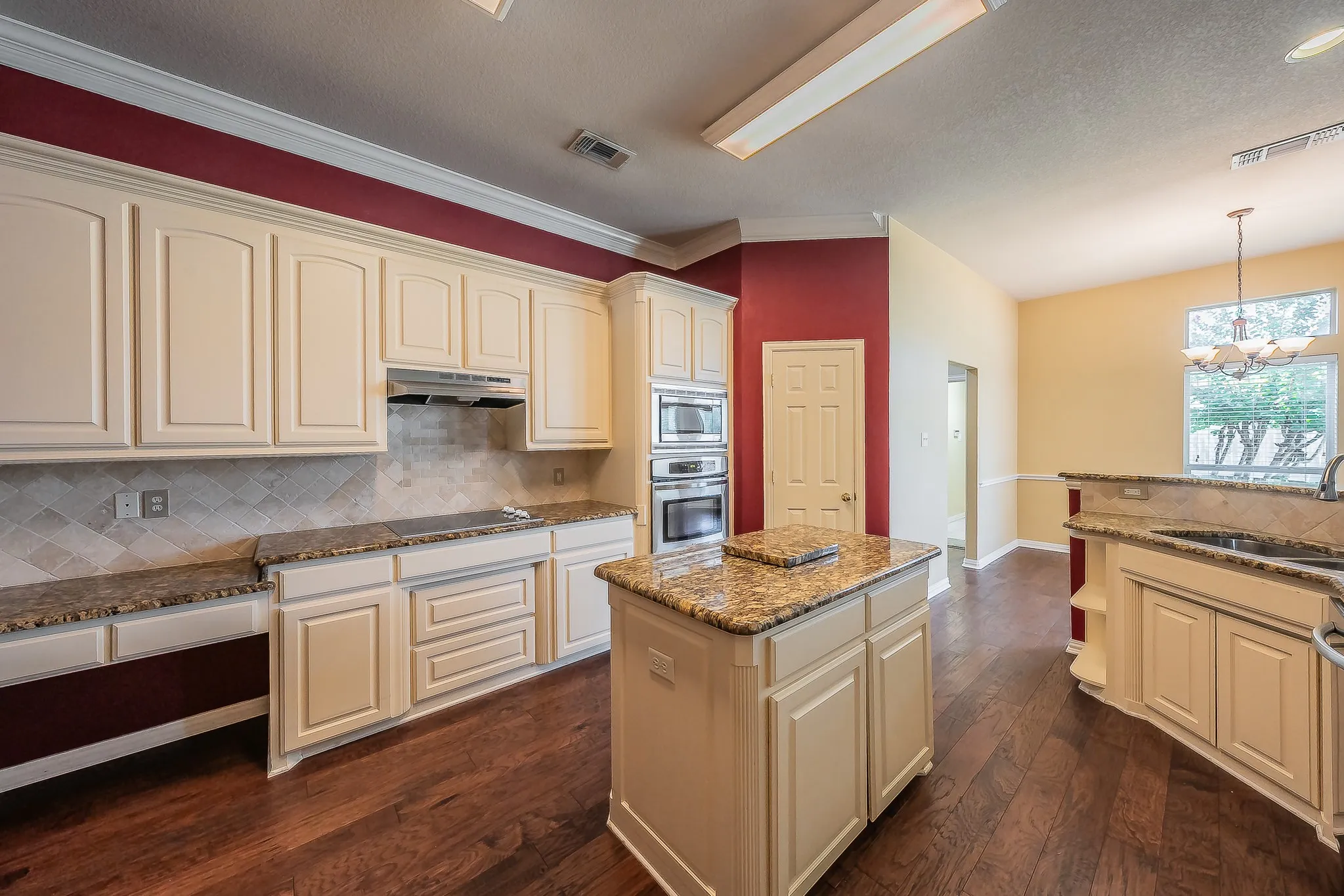 Kitchen featuring wood-finish flooring, cream cabinetry, a center island with a stone countertop, built-in stainless steel appliances, and a tiled backsplash