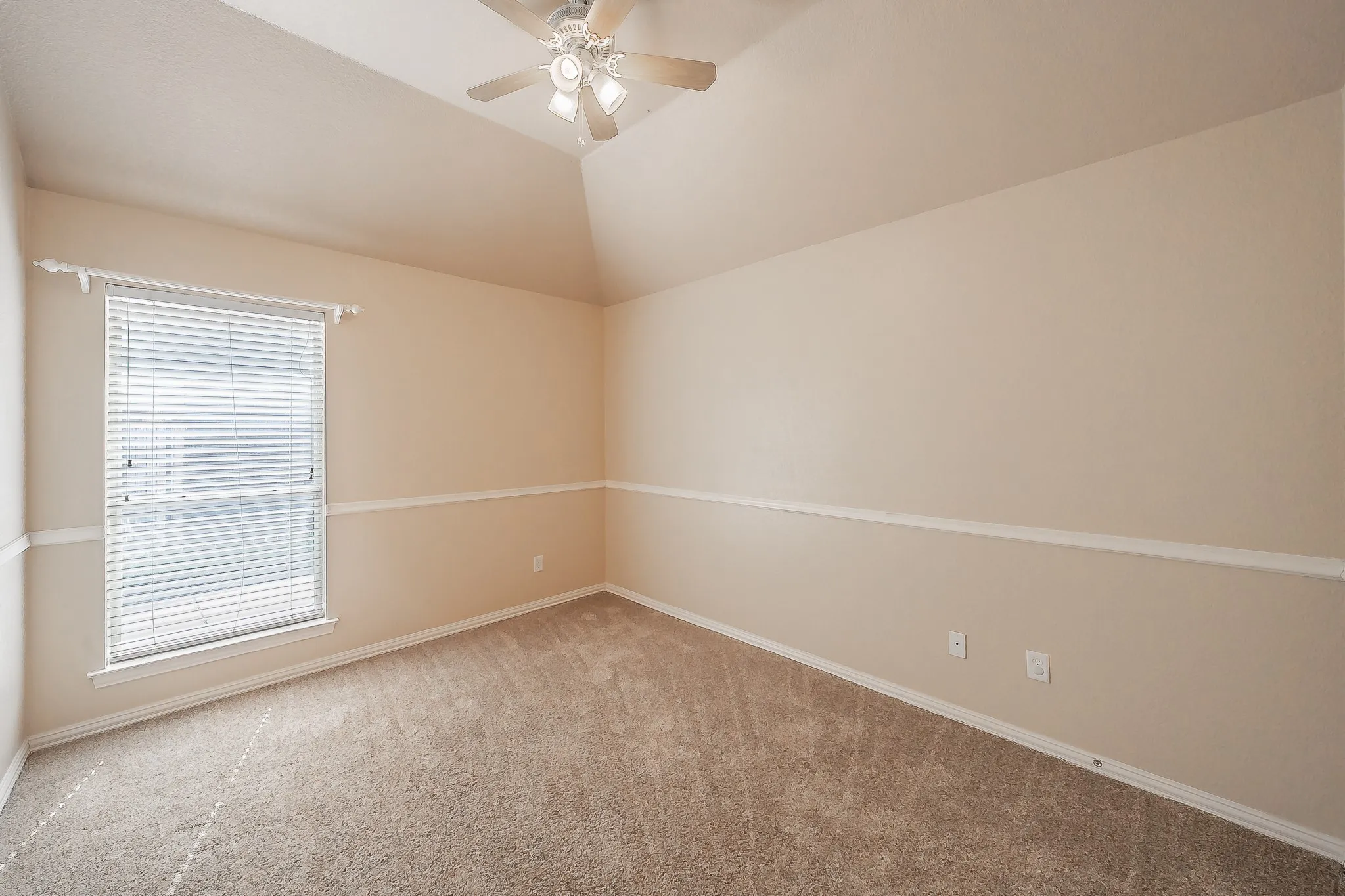 Vaulted ceiling, ceiling fan, neutral carpet, single window with blinds, and decorative chair rail molding