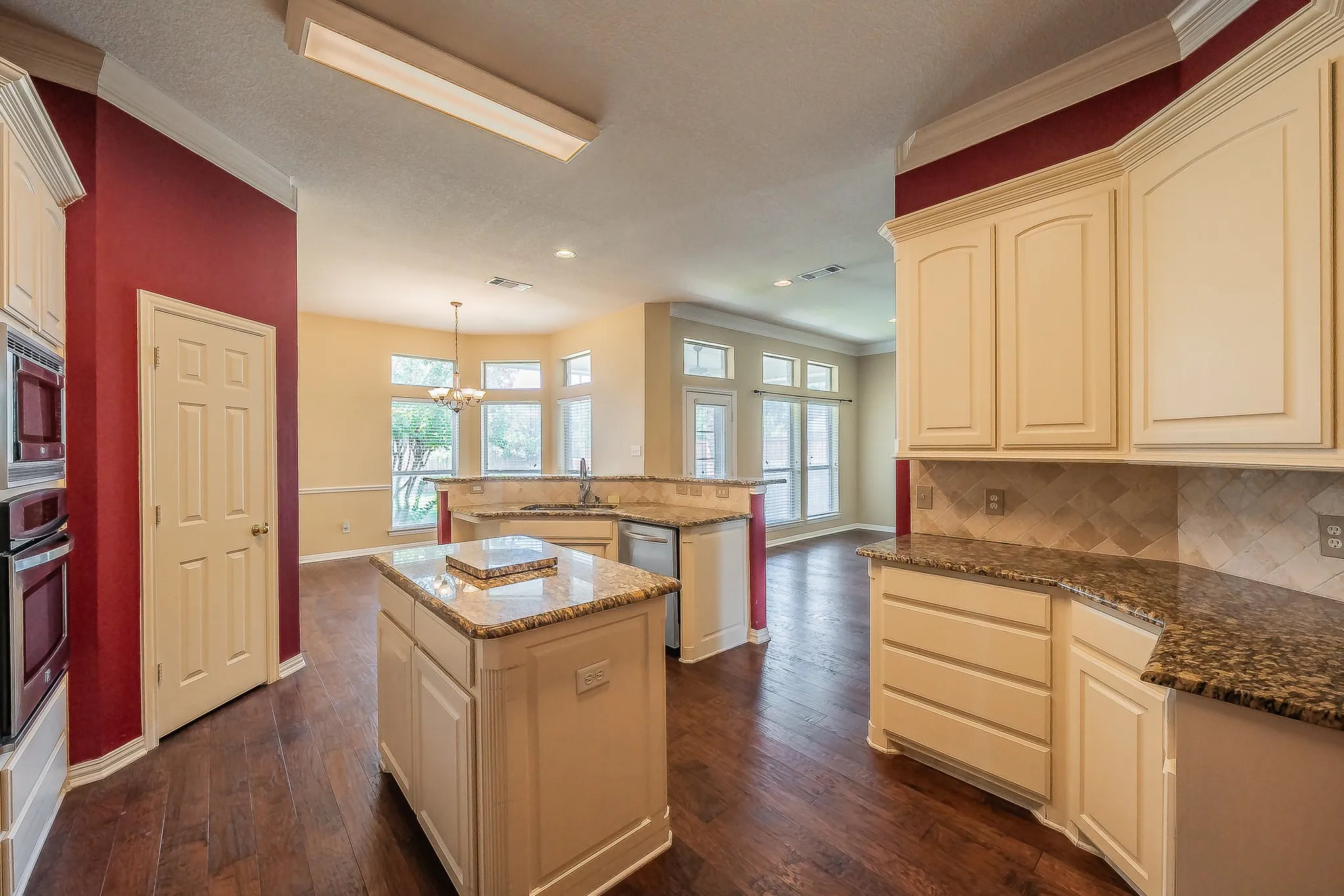 Kitchen featuring extensive light-toned cabinetry, built-in double ovens, dark wood-finish flooring, granite countertops, and a tile backsplash