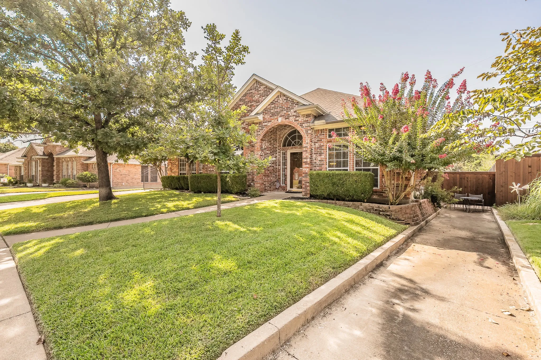 Brick exterior with arched entry, mature trees, manicured lawn, and established landscaping