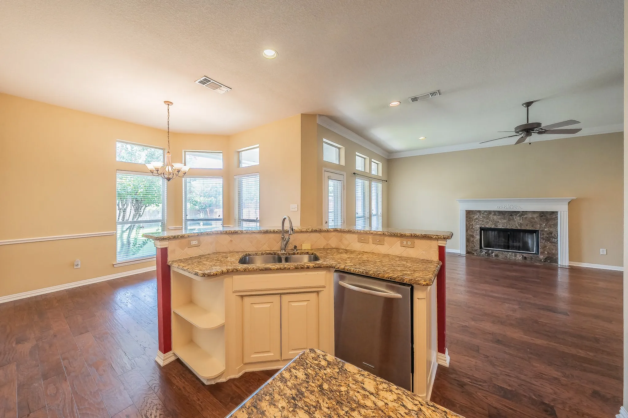 Open-concept living space with wood-finish flooring, a kitchen island with granite countertops, and a built-in stainless steel dishwasher