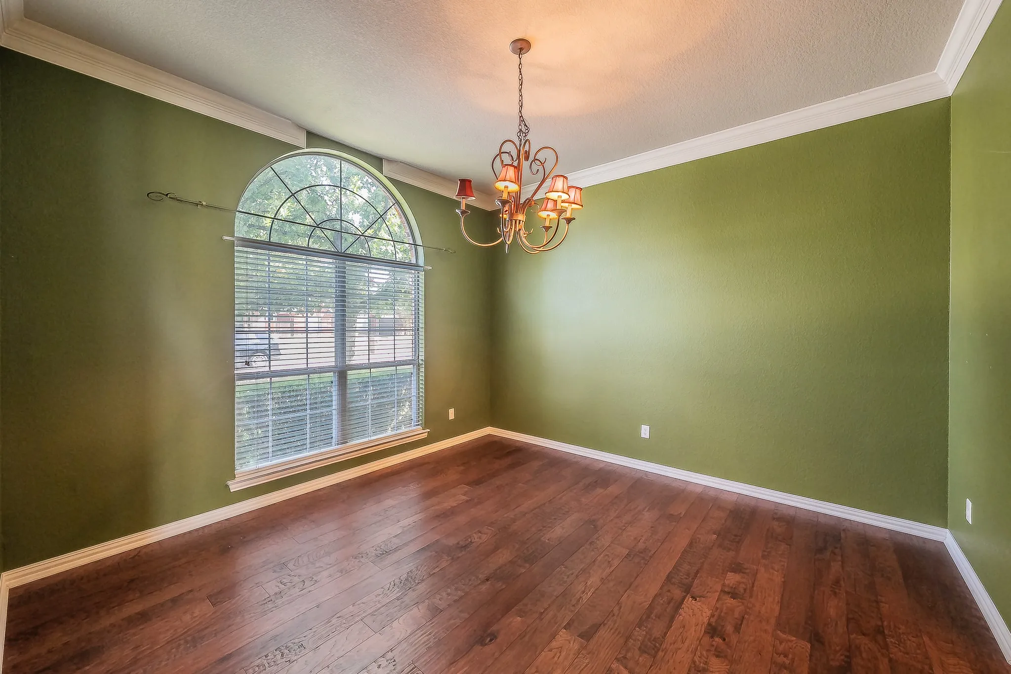 Hardwood-style flooring, arched window with blinds, decorative chandelier, and crown molding