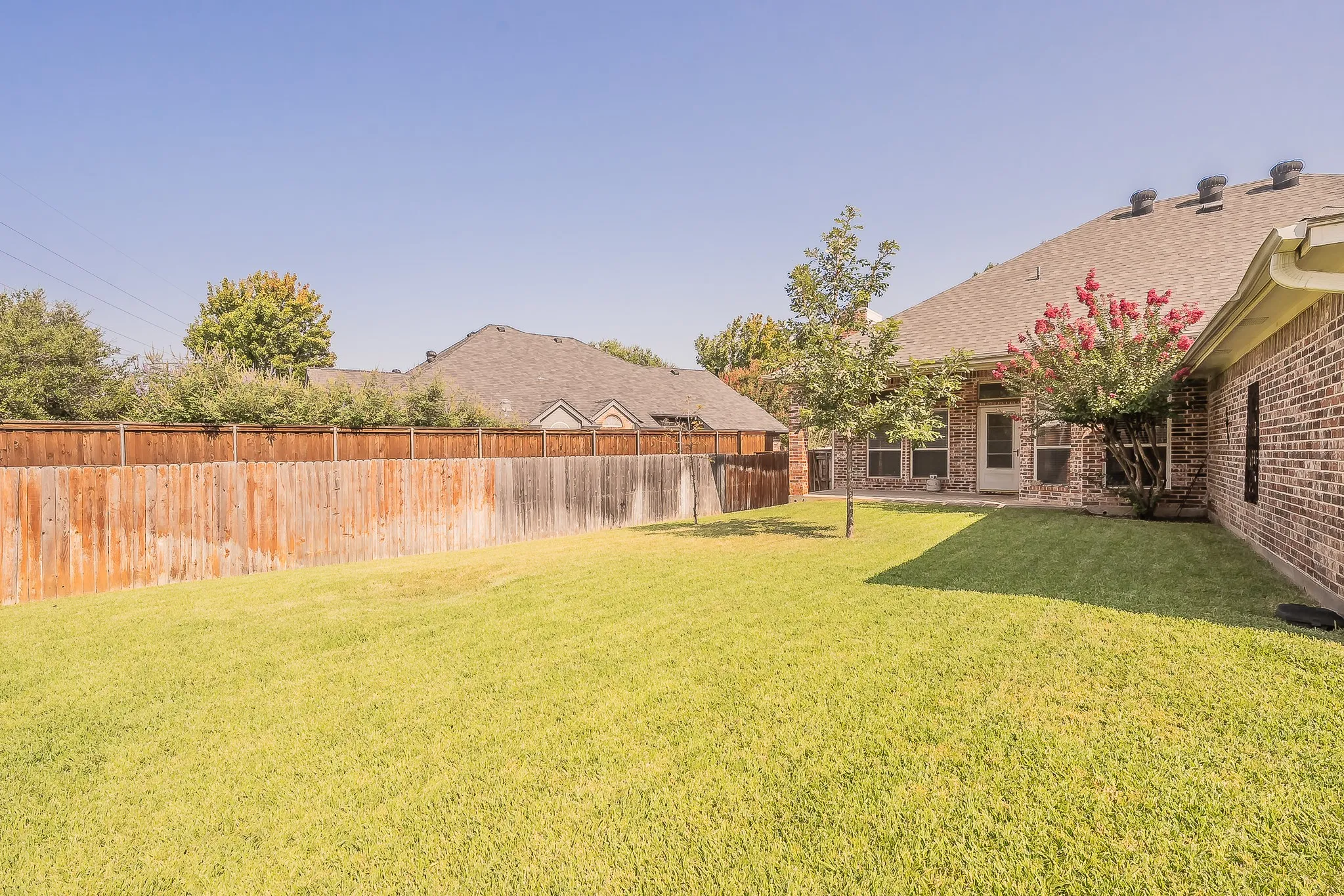 Expansive green lawn, wood fence, brick exterior, covered patio, and mature landscaping