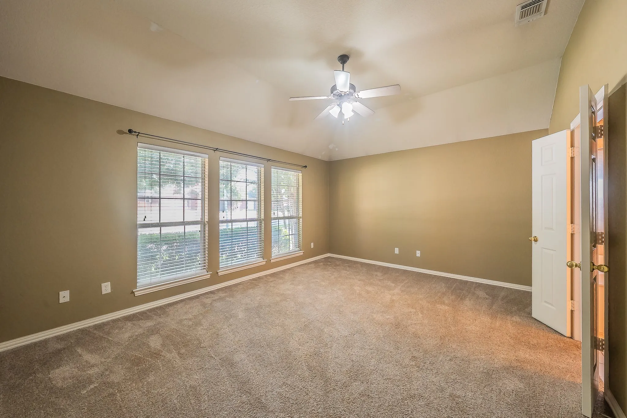 Vaulted ceiling, ceiling fan, triple windows with blinds, neutral carpet flooring, and a paneled interior door