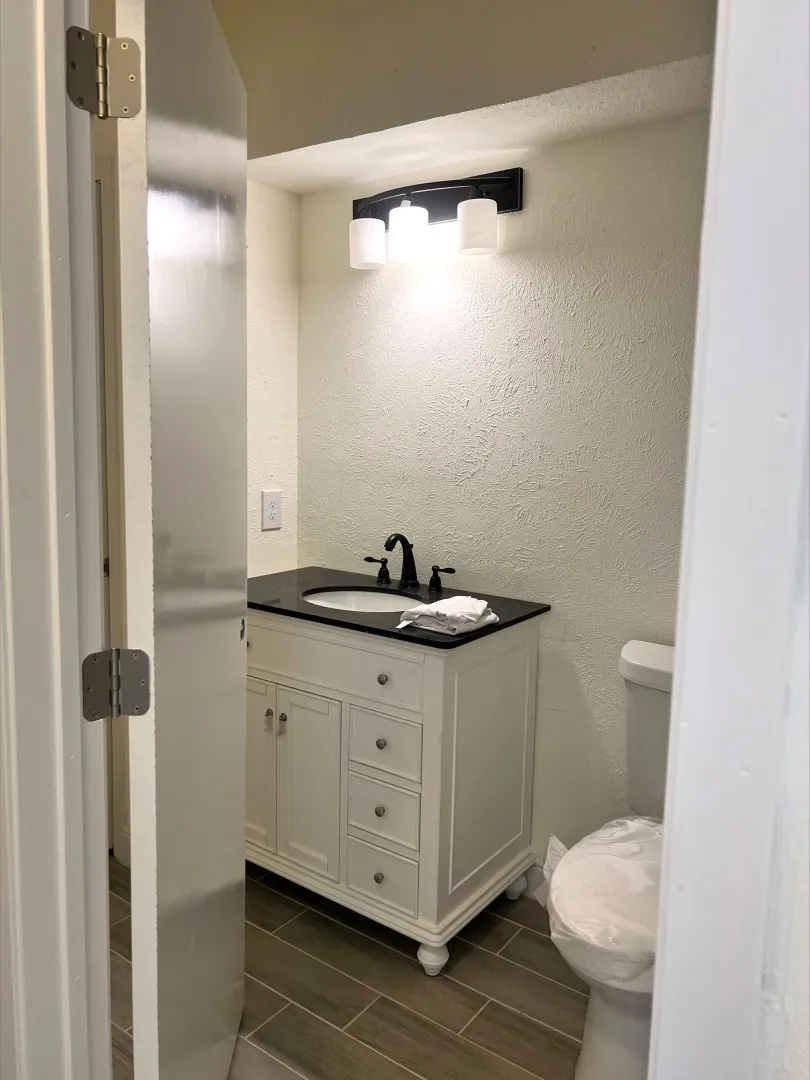White vanity with a dark countertop and undermount sink, dark-finished faucet, and sconce lighting