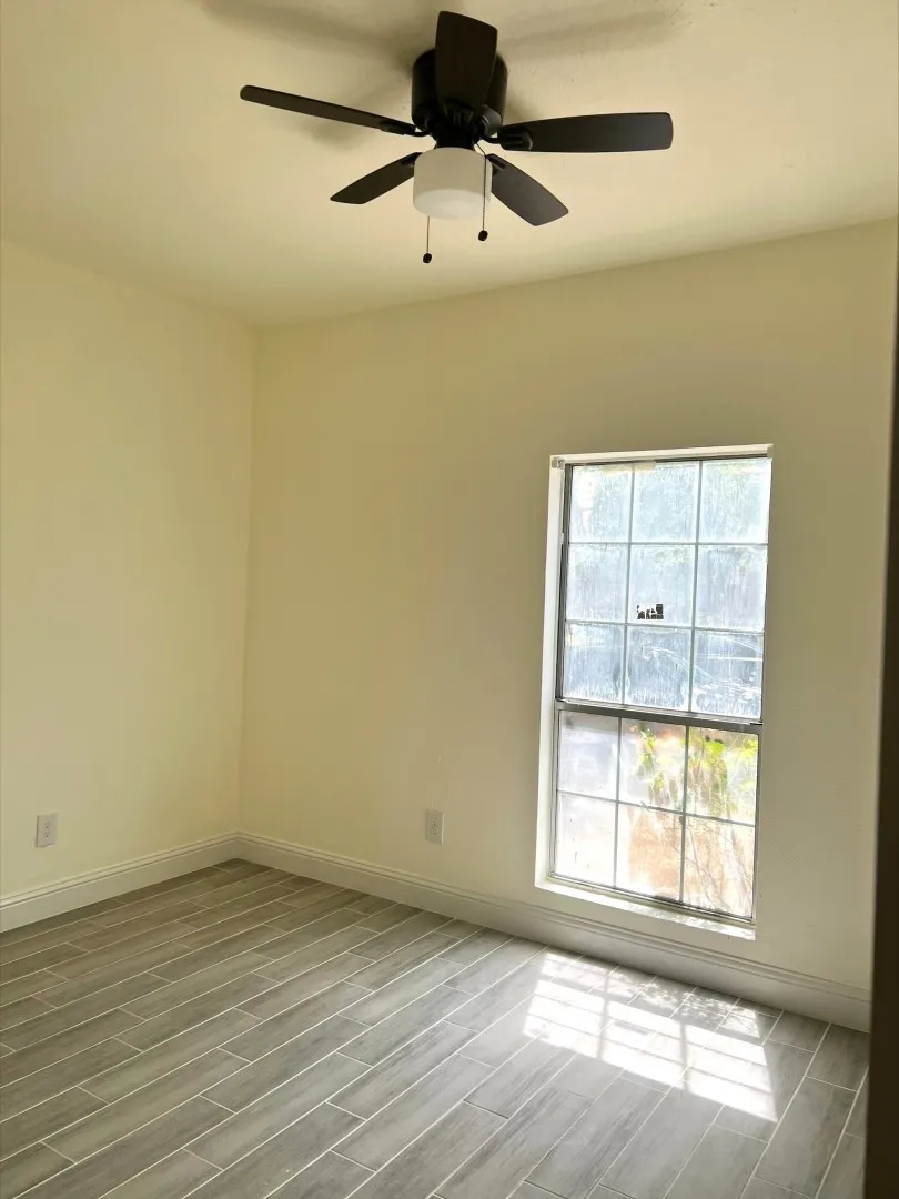 Rectangular window, overhead ceiling fan with lighting, and wood-finish tile flooring
