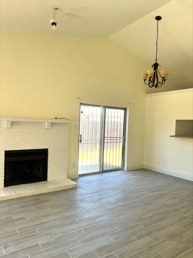 Vaulted ceiling with an installed chandelier, brick fireplace, wood-finish tile flooring, and sliding glass door