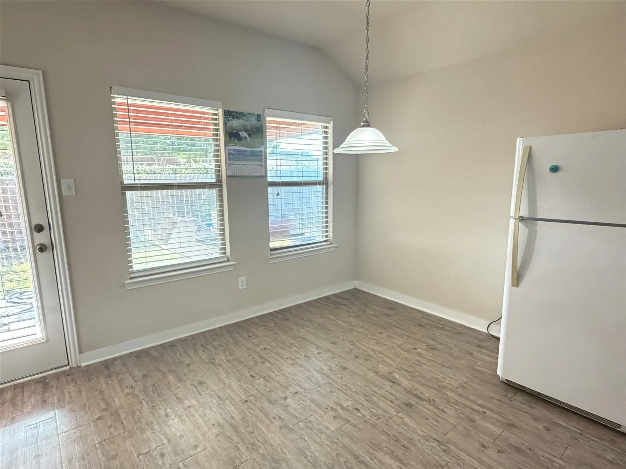Vaulted ceiling with pendant lighting, wood-finish flooring, and multiple windows with blinds