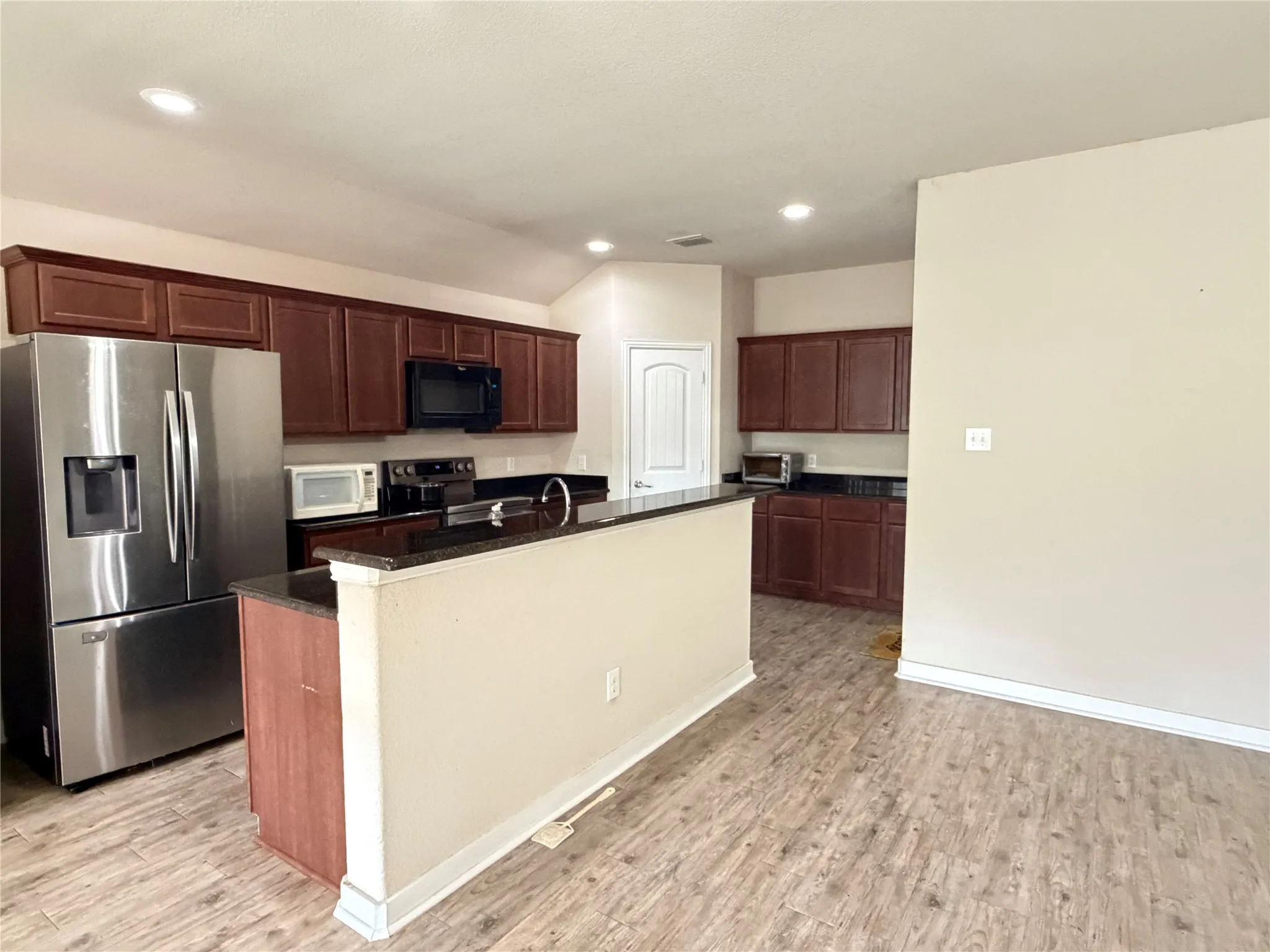 Kitchen featuring wood-finish flooring, dark wood cabinetry, black countertops, and stainless steel appliances