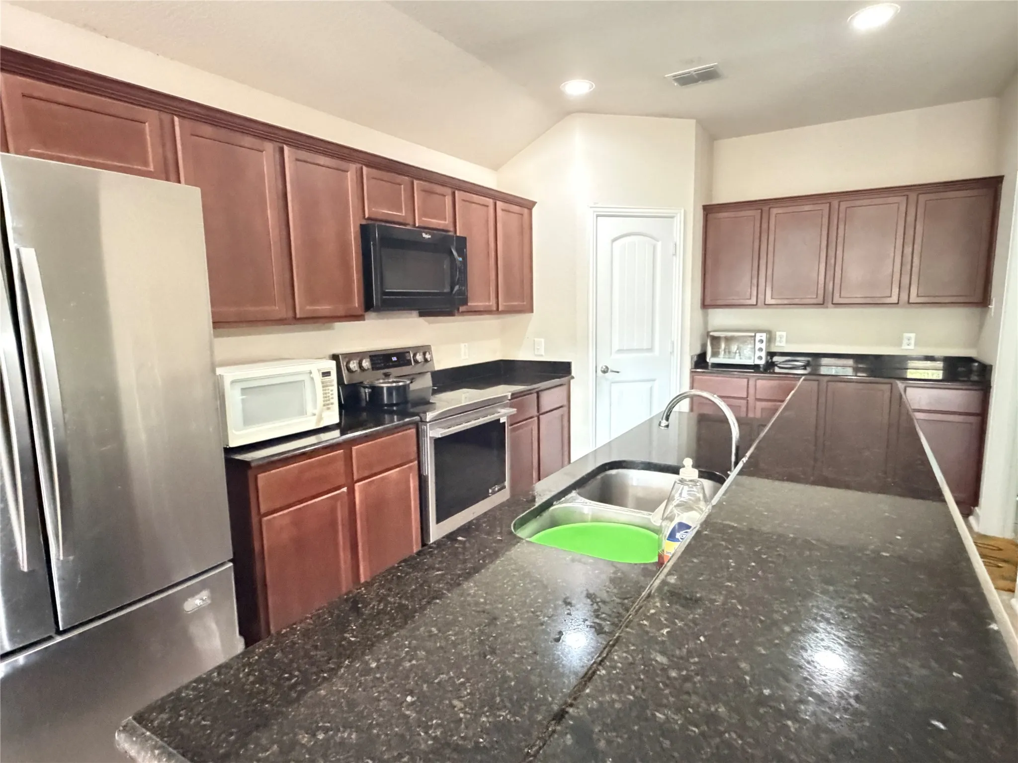 Kitchen featuring dark wood-finish cabinetry, dark speckled countertops, and stainless steel appliances