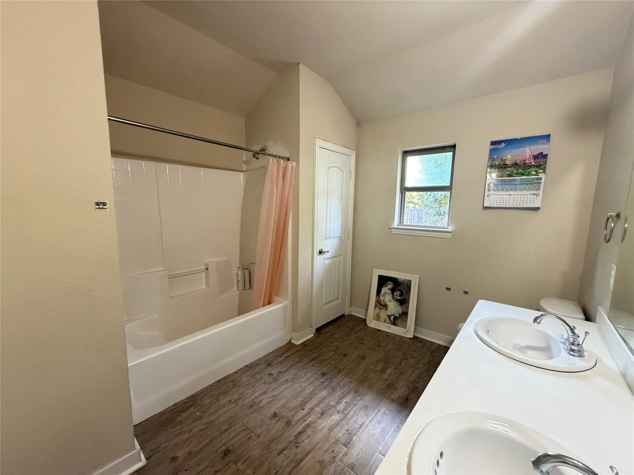 Wood-finish flooring, dual vanity with undermount sinks, single window, and a shower/tub combination
