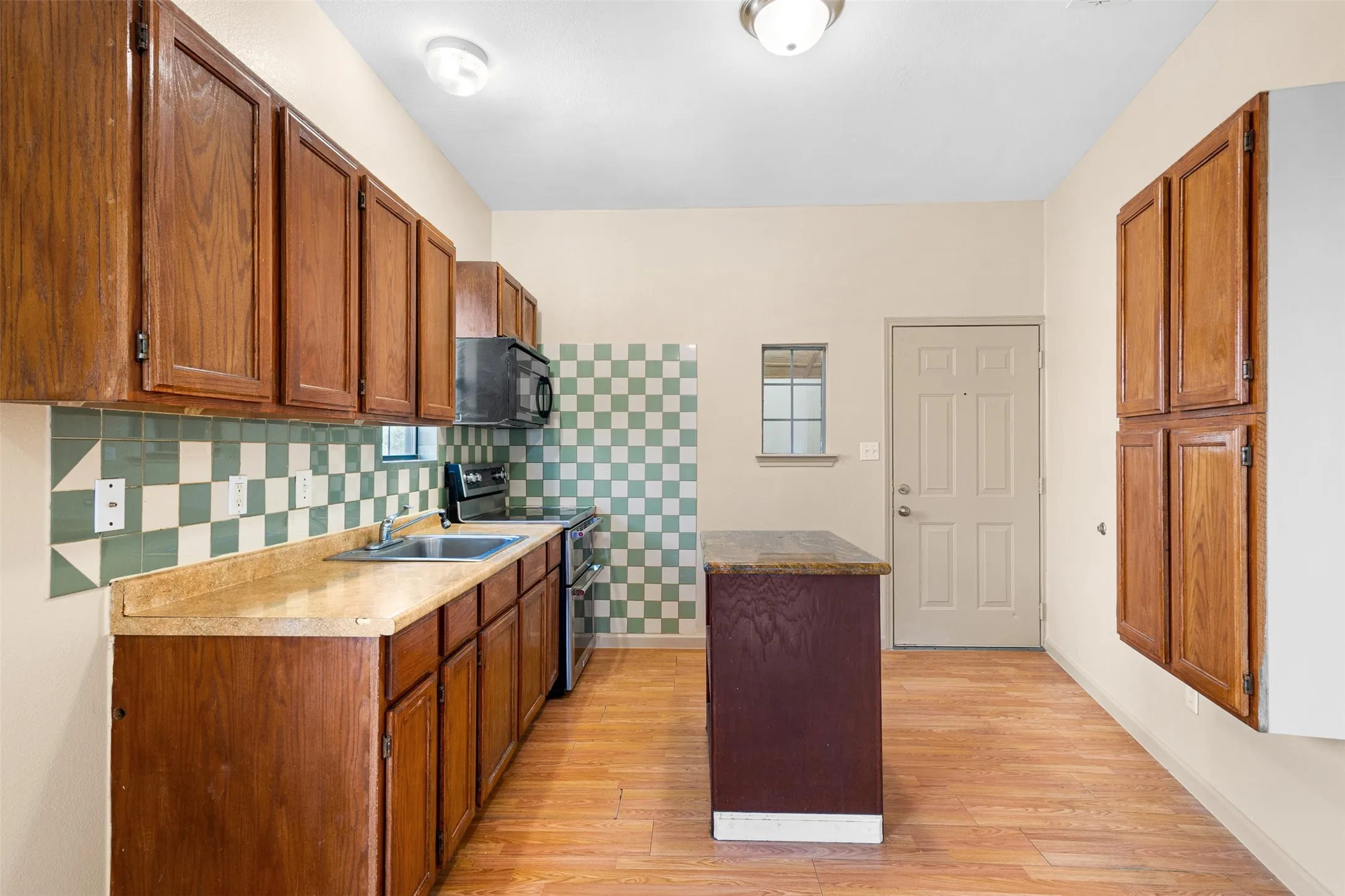 Kitchen featuring wood-finish flooring, wood cabinetry, stone-finish countertops, checkerboard tile backsplash, and a central island