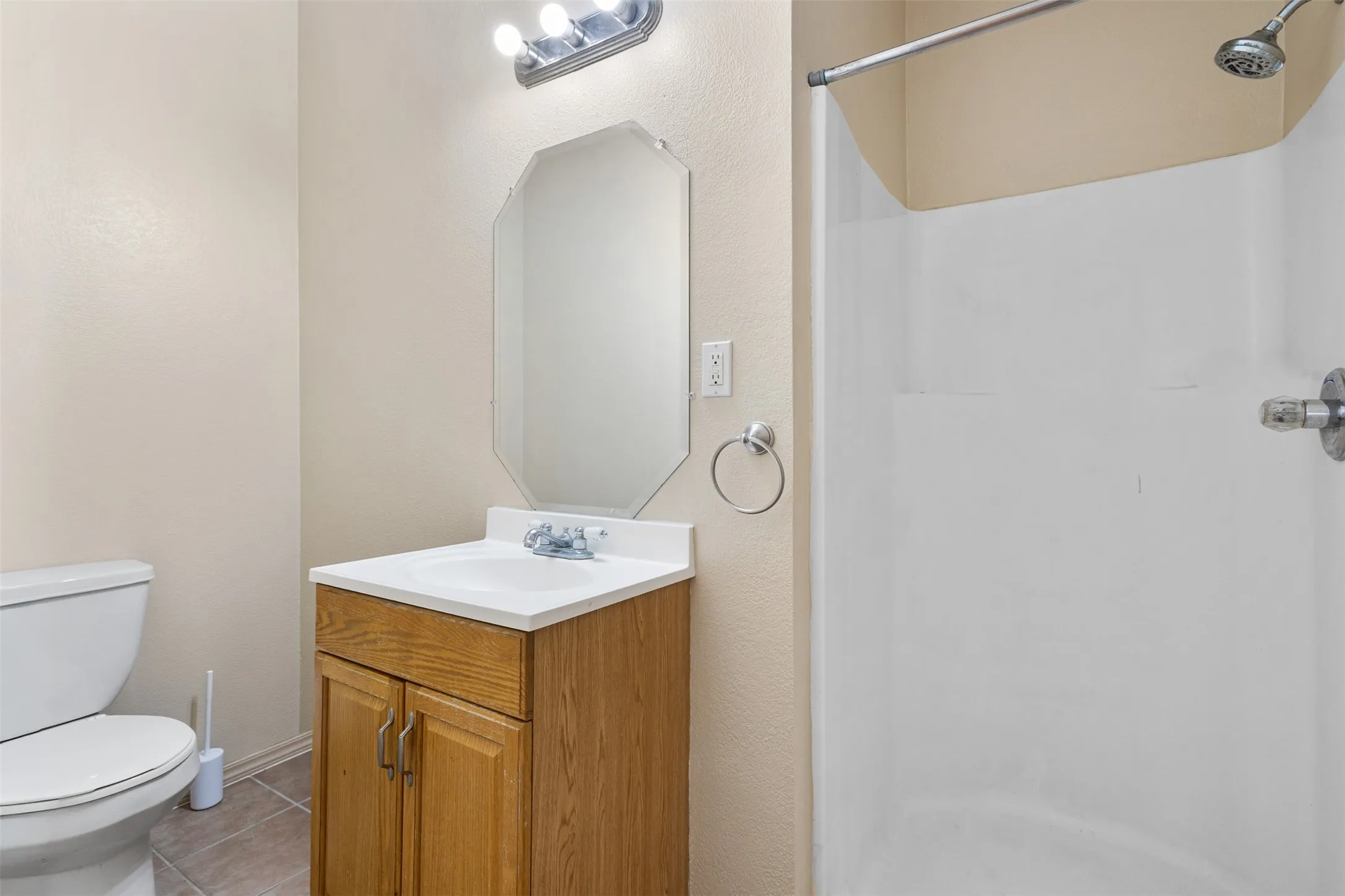 Full bathroom featuring a wood-finish vanity, integrated sink, and an octagonal mirror