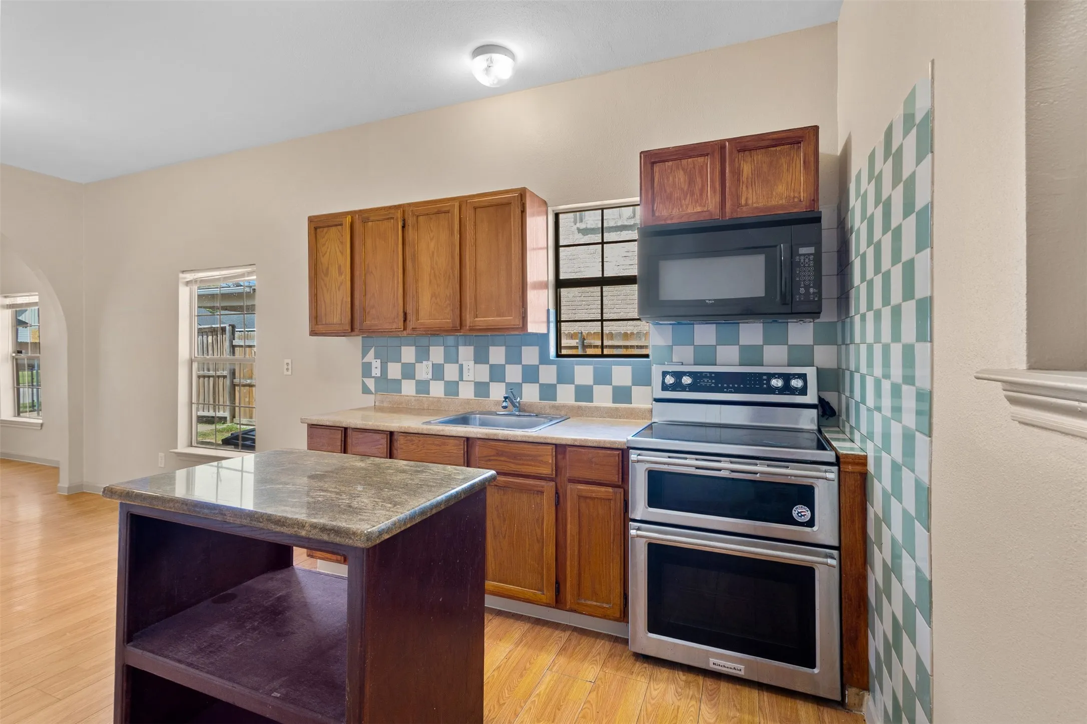 Kitchen featuring wood cabinetry, stainless steel double oven, black microwave, a kitchen island with a stone-finish countertop, and wood-finish flooring