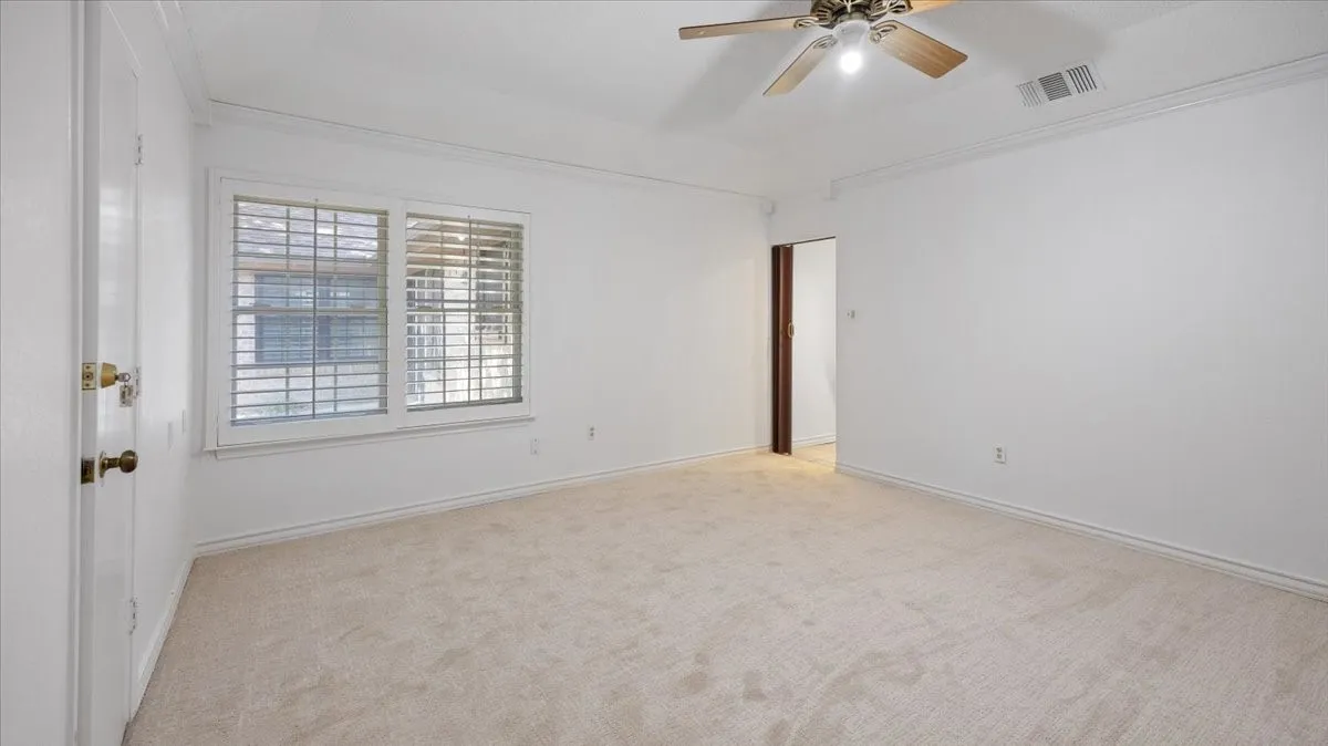 Spacious room with plush carpeting, crown molding, and a ceiling fan