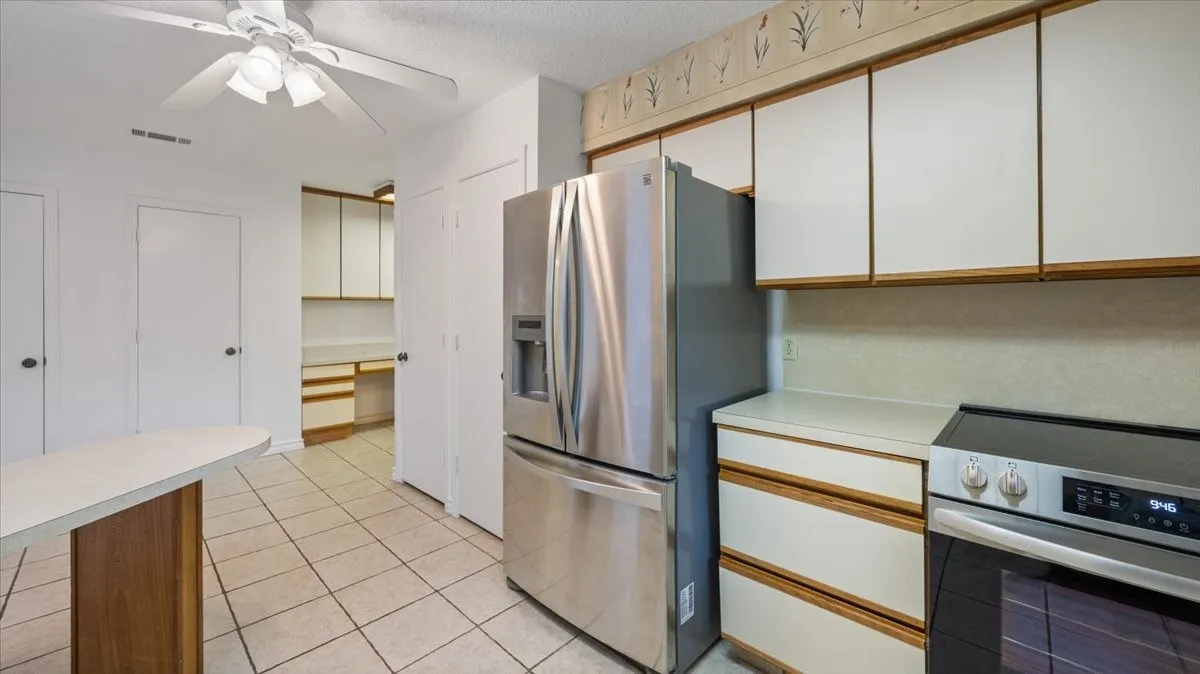 Kitchen featuring a stainless steel refrigerator, white cabinetry, a built-in electric range, and tile flooring