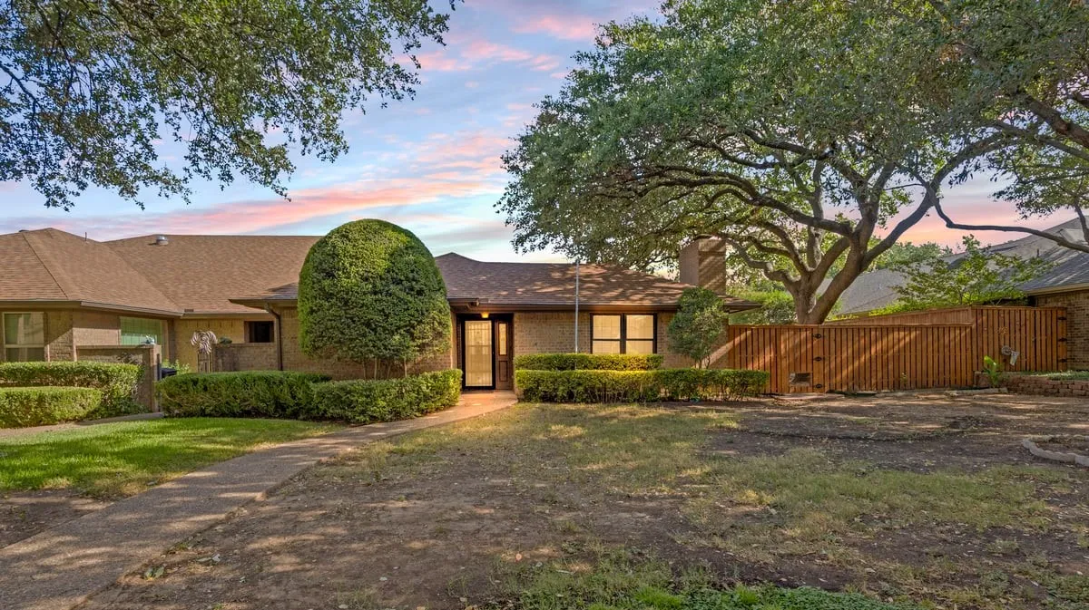 Single-story residence featuring a brown shingle roof, brick exterior, and mature landscaping